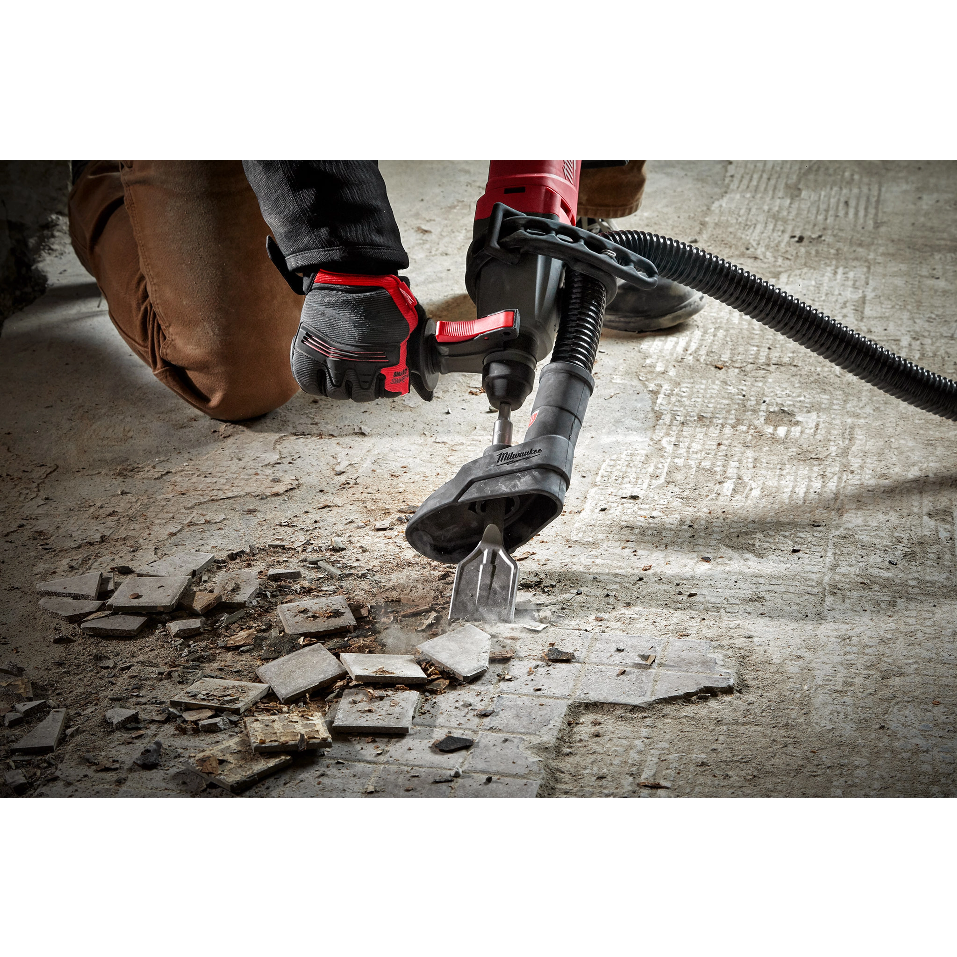 Person using the SDS+ SLEDGE 1-7/8" Tile Chisel with a power tool to remove tiles from a concrete floor, debris scattered around.
