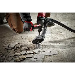 Person using the SDS+ SLEDGE 1-7/8" Tile Chisel with a power tool to remove tiles from a concrete floor, debris scattered around.