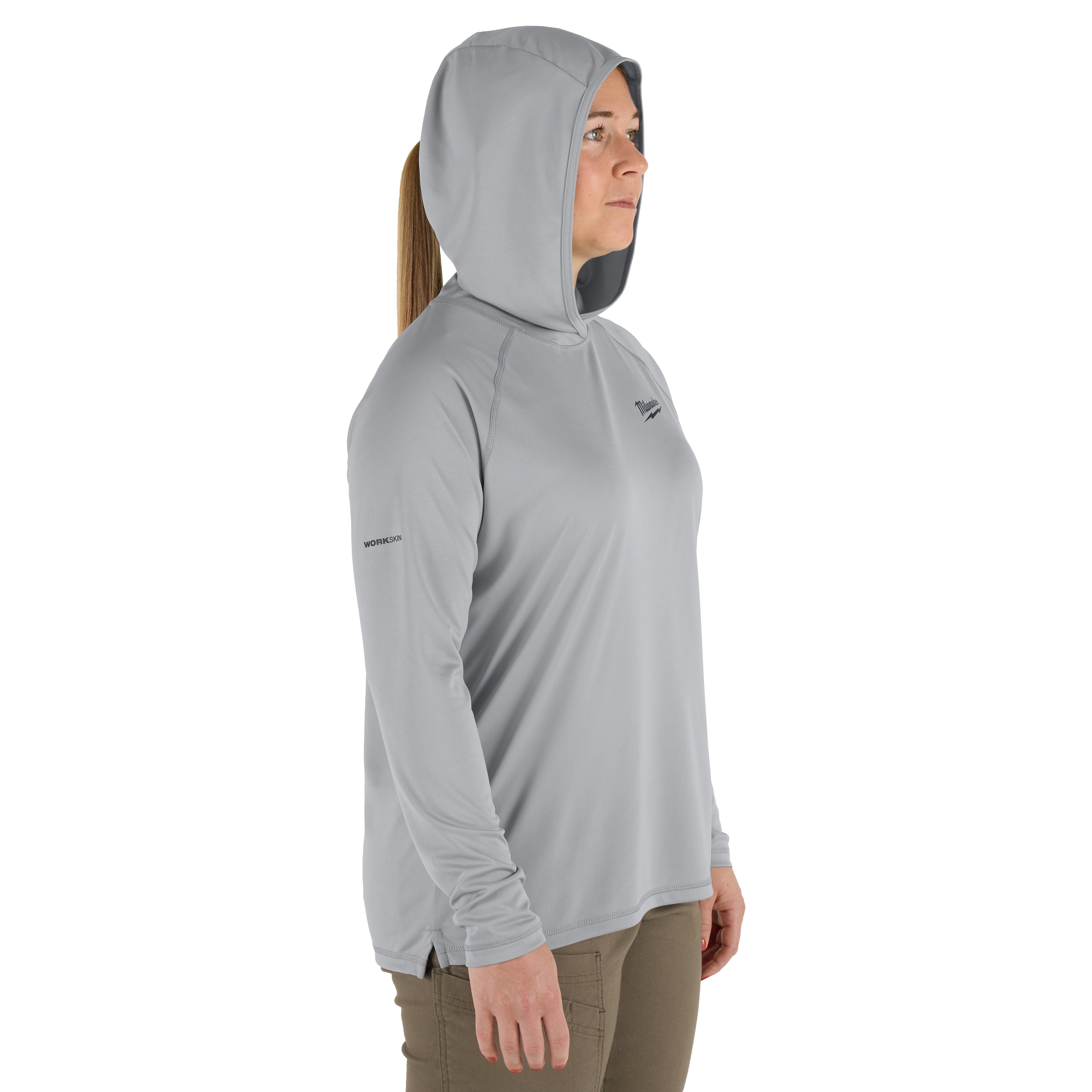 The Women's WORKSKIN Hooded Sun Shirt – Gray is shown. The lightweight, long-sleeve hoodie is designed for sun protection and comfort. It features moisture-wicking fabric and a hood for added coverage. The model wears tan pants with a hoodie.