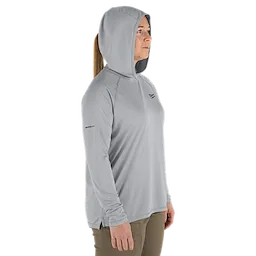 The Women's WORKSKIN Hooded Sun Shirt – Gray is shown. The lightweight, long-sleeve hoodie is designed for sun protection and comfort. It features moisture-wicking fabric and a hood for added coverage. The model wears tan pants with a hoodie.