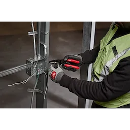 A person in work gloves uses a 10-28 AWG Multi-Purpose Dipped Grip Wire Stripper & Cutter with Reinforced Head to strip wires on a metal frame structure.
