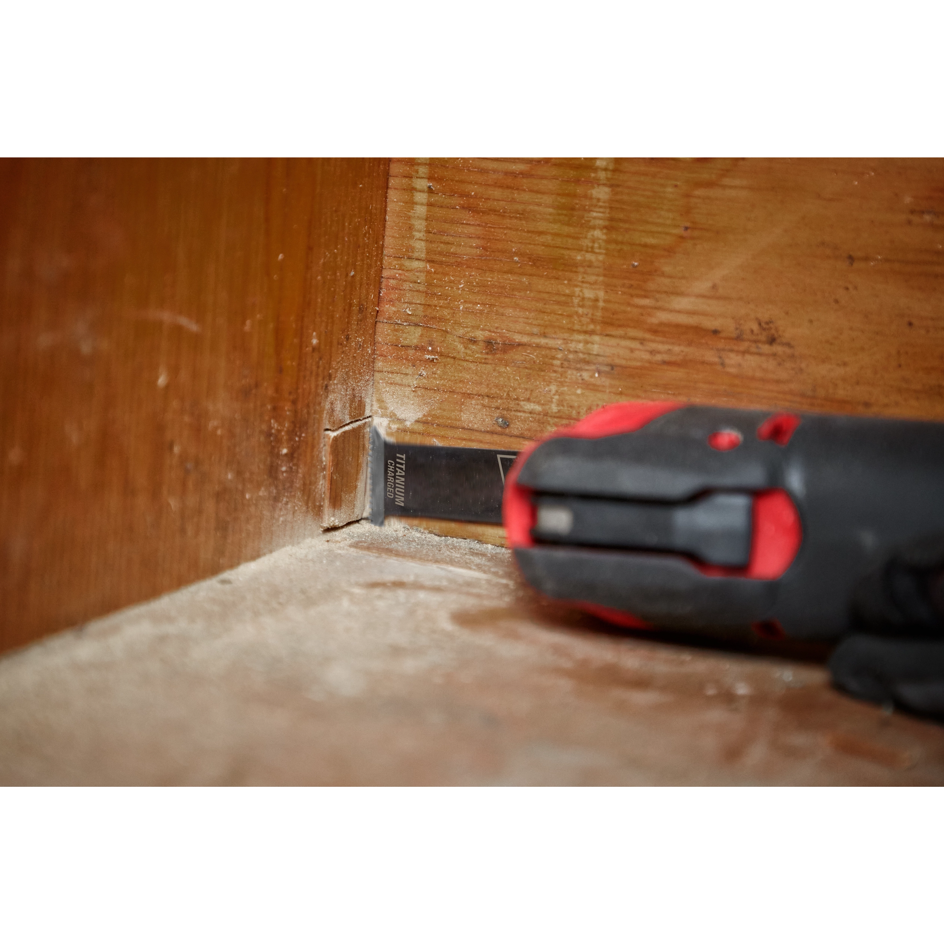 Milwaukee Open-Lok 1-1/4" Titanium Charged Bi-Metal Multi-Material Multi-Tool Blade cutting into the bottom of a wooden wall.