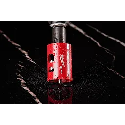 The image shows a Milwaukee® 1-3/8" DIAMOND MAX™ Hole Saw with a red cylindrical body. The tool is attached to a drill and is placed on a shiny black surface with water drops. The name and branding are visible on the side of the hole saw.