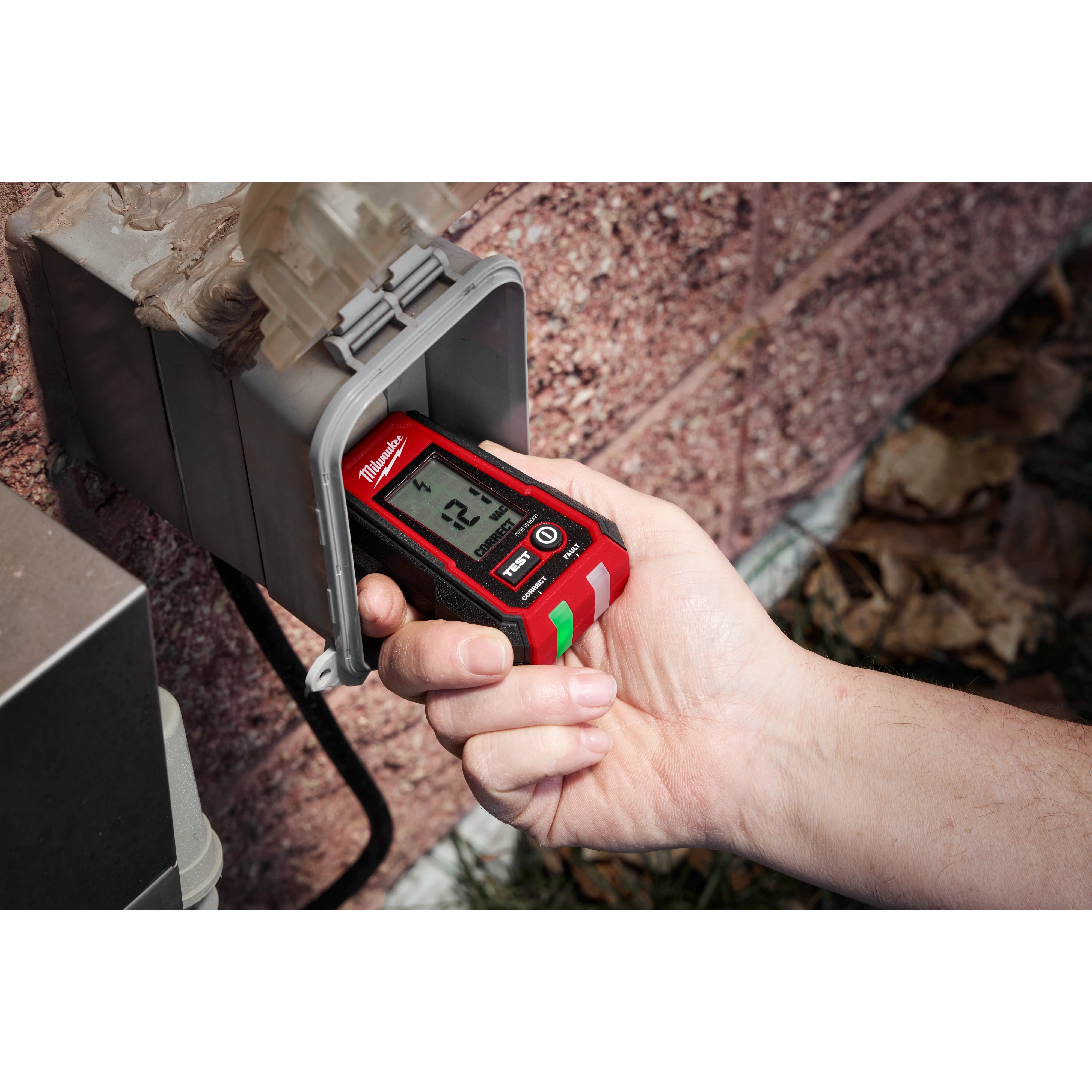 A hand is holding a Digital GFCI Receptacle Tester, inserting it into an outdoor power outlet. The device displays a reading on its digital screen, indicating its function in testing electrical outlets for safety and functionality.