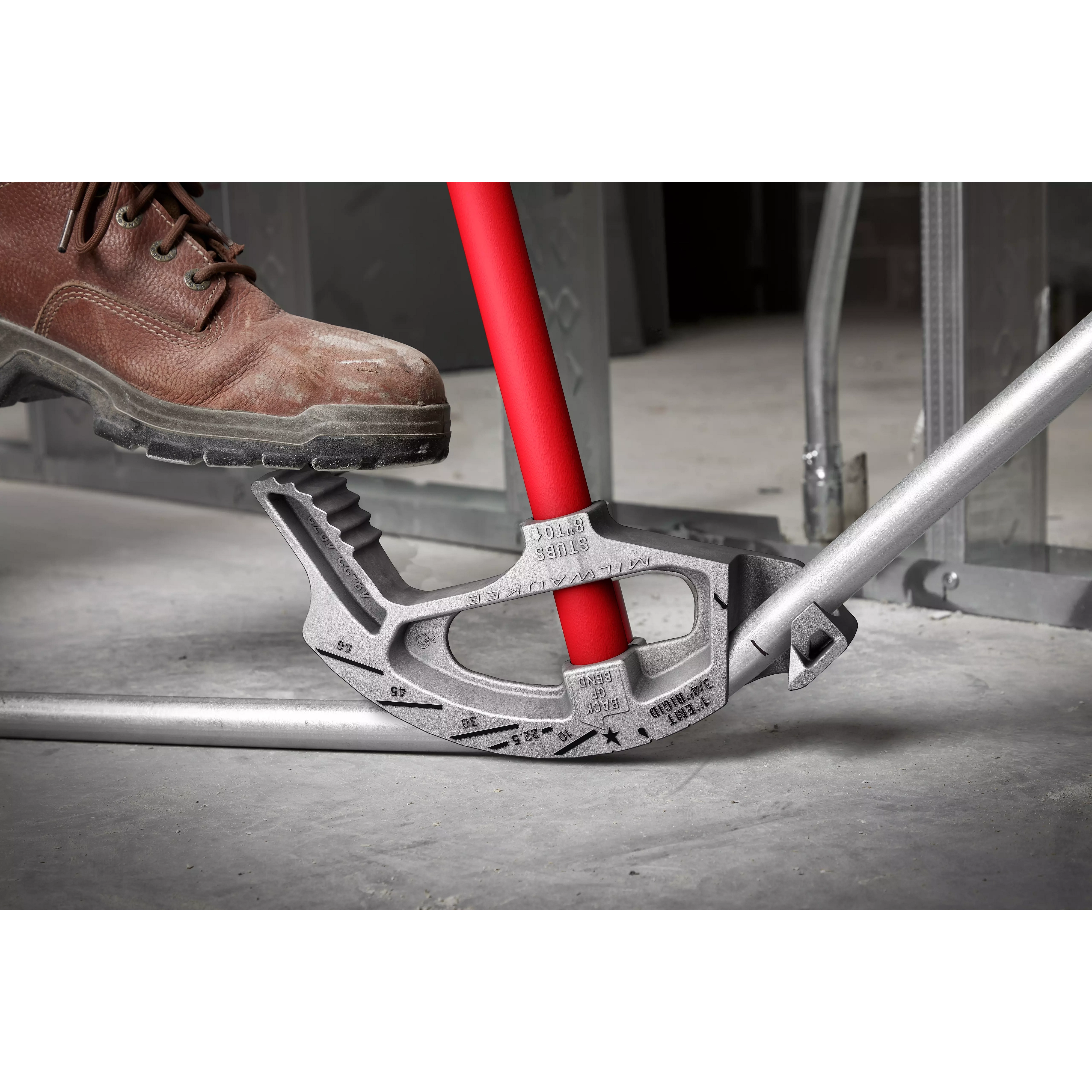 A boot using Offset Jobsite Scissors to cut through a metal pipe on a concrete floor.