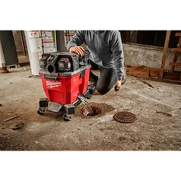 Person using a red 9 Gallon Wet/Dry Vacuum Tank to clean a concrete floor, draining water into a floor drain.