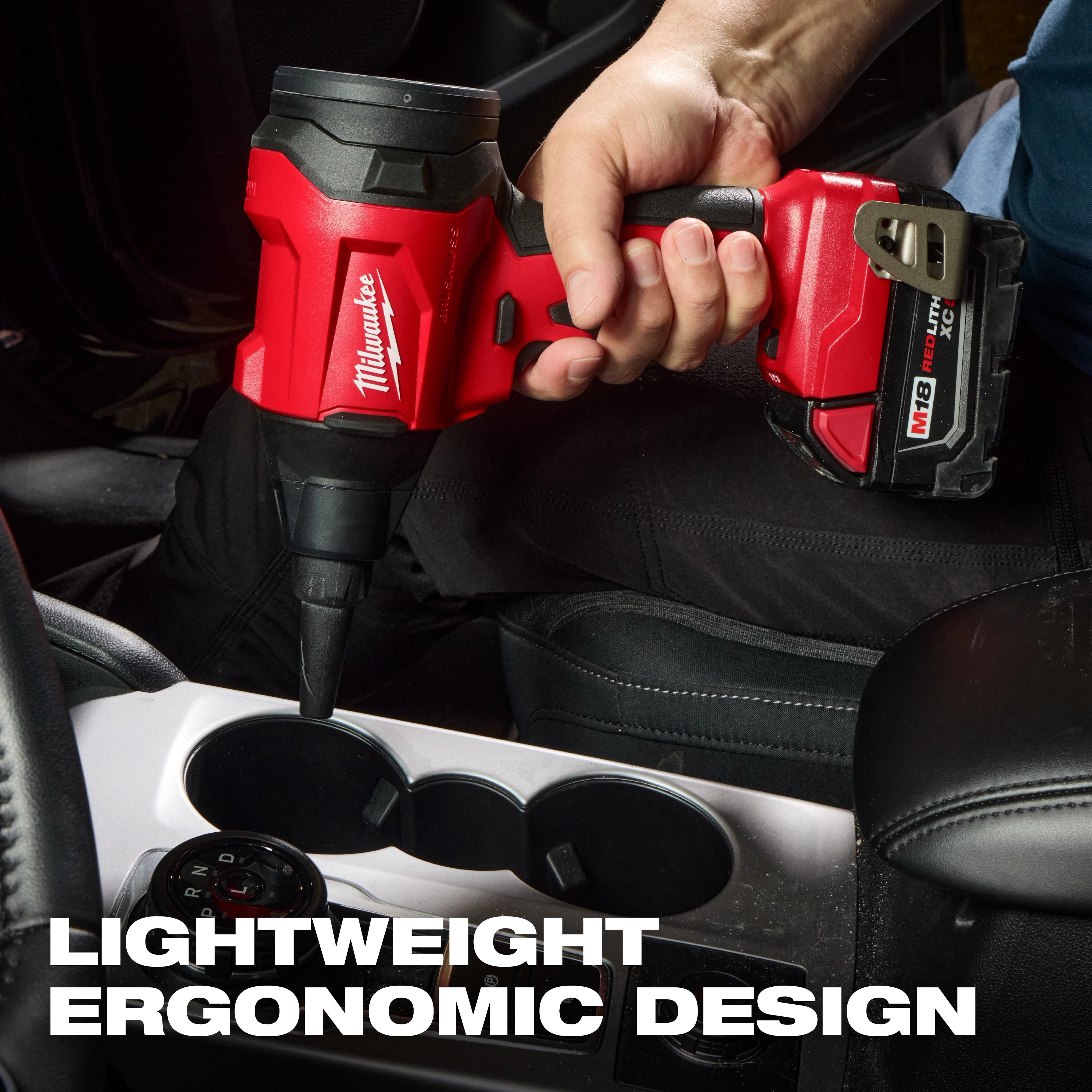 A person uses the M18™ Brushless Precision Blower to clean a car's cupholder area. The tool is red and black with "Milwaukee" branding, featuring a lightweight ergonomic design.