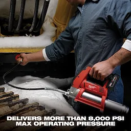 A person operates a Milwaukee cordless grease gun under snowy industrial equipment. The grease gun, held in the person's right hand, is connected to a hose. Text at the bottom reads, "Delivers more than 8,000 PSI max operating pressure."