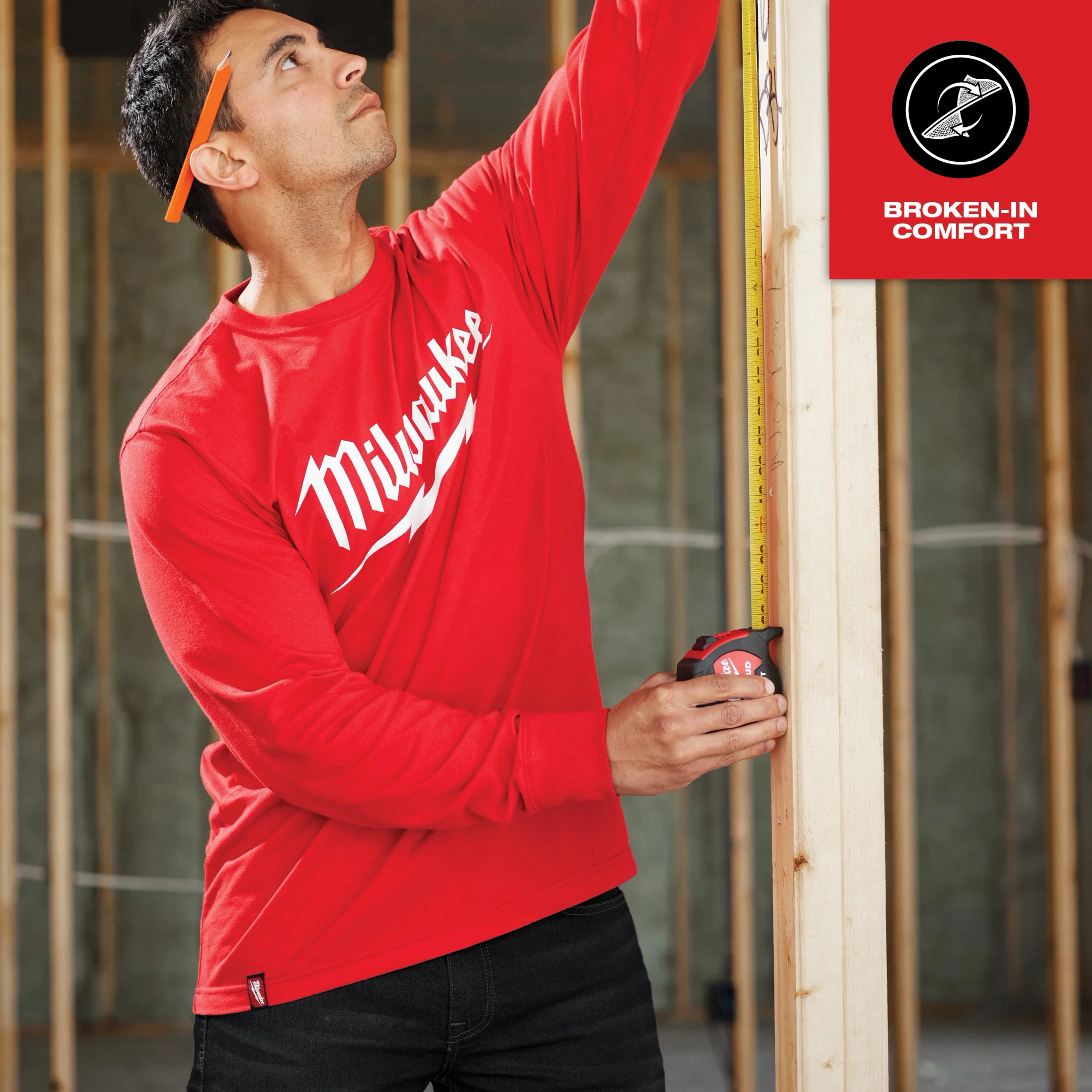 Man measuring wooden frame while wearing Heavy Duty Tee - Long Sleeve Logo Feature Shot in red with white logo. "Broken-In Comfort" text in the corner.