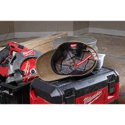 Waxed Canvas Adjustable Hat with a plaid inner lining displayed open on a toolbox, surrounded by power tools and construction materials.