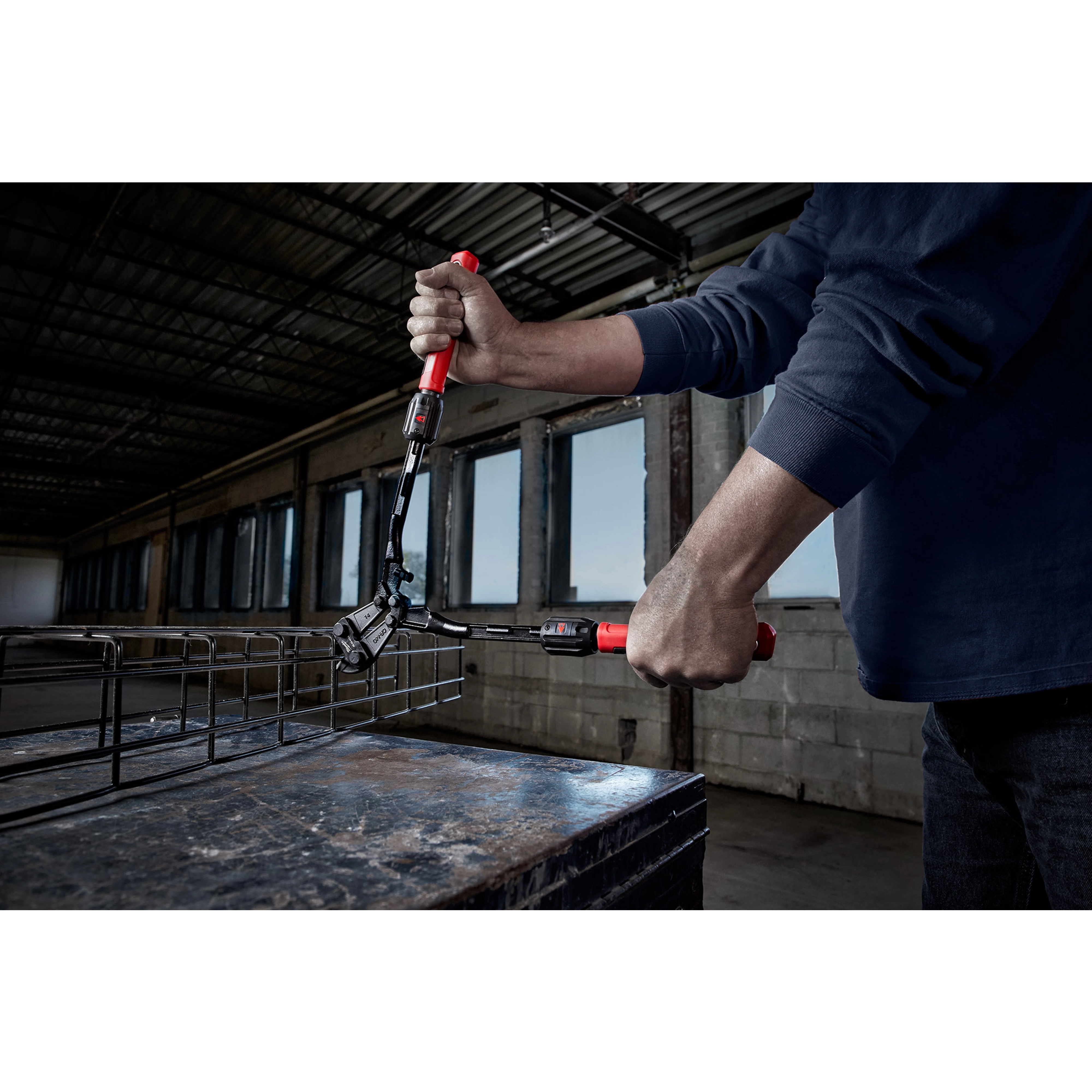 Person using the 14" Adaptable Bolt Cutter with POWERMOVE Extendable Arms to cut through metal in an industrial setting.