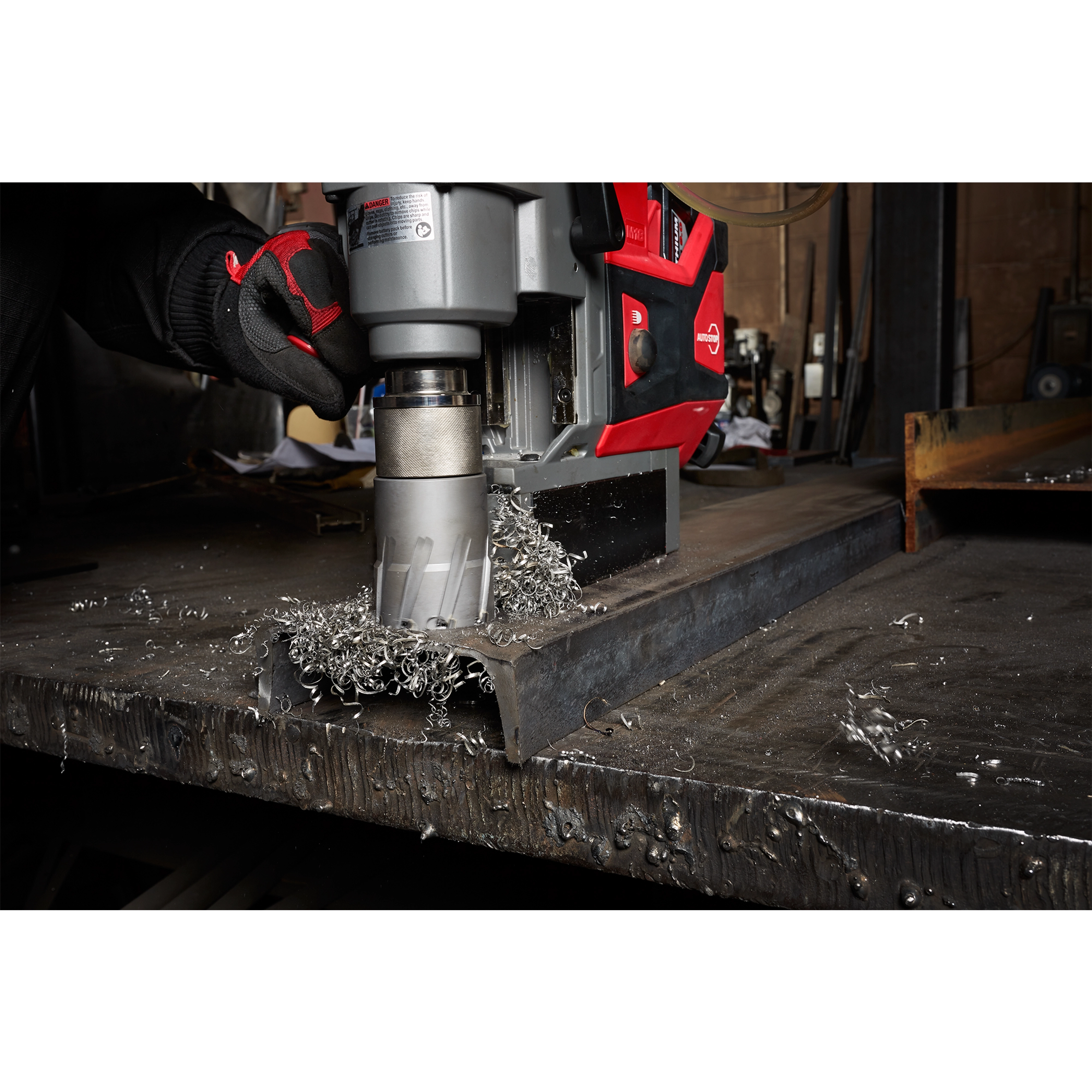 Worker using Annular Cutter attached to a red and gray machine to drill through a thick metal sheet, producing metal shavings.