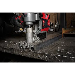 Worker using Annular Cutter attached to a red and gray machine to drill through a thick metal sheet, producing metal shavings.