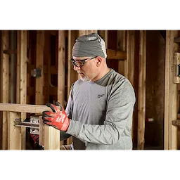 Person working indoors wearing a long-sleeve shirt, red gloves, and gray WORKSKIN Performance Neck Gaiter, handling a tool.