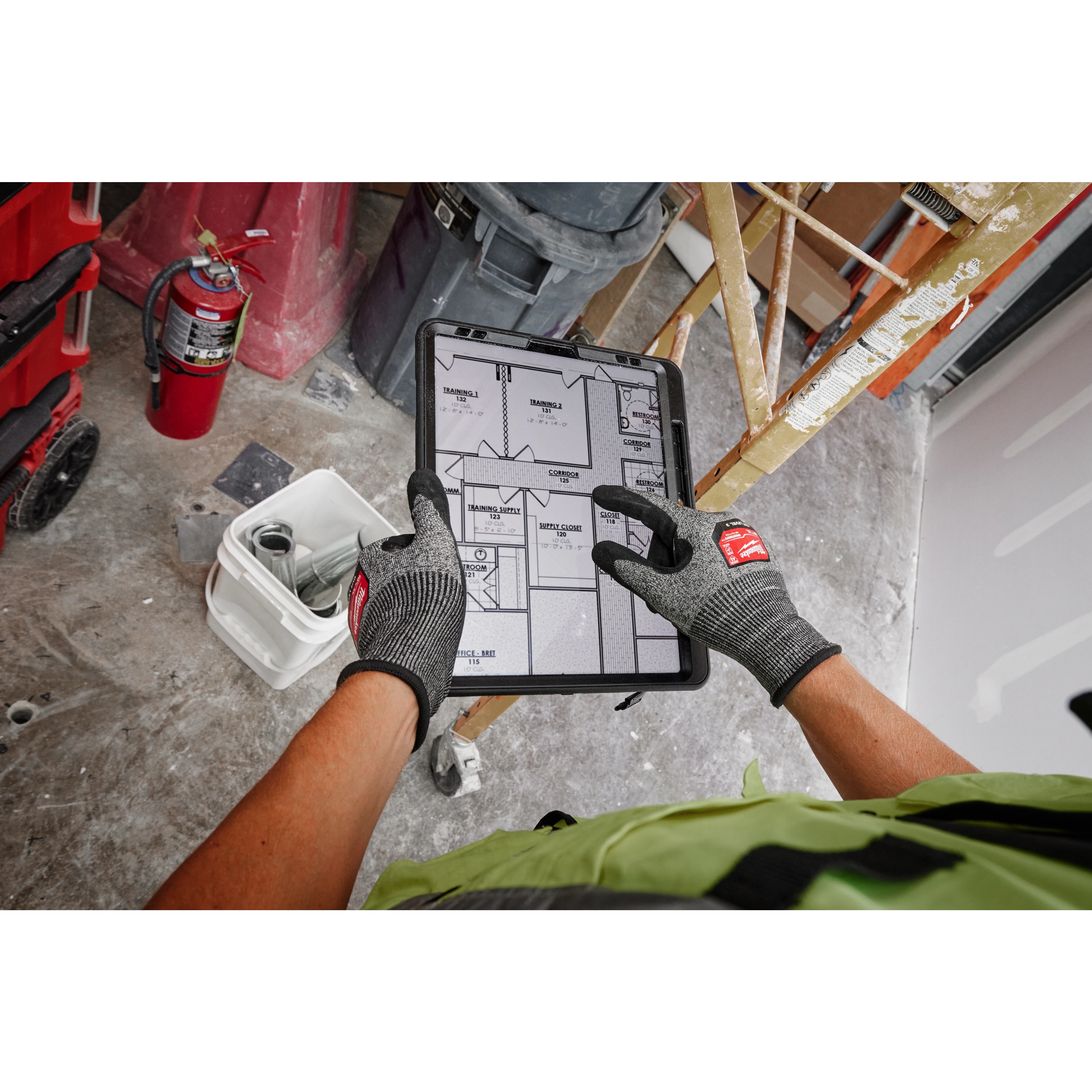 Person wearing Cut Level 3 High-Dexterity Nitrile Dipped Gloves - XL, holding a tablet with construction plans on a job site.