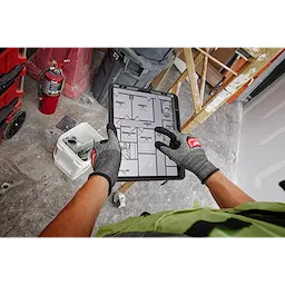 Person wearing Cut Level 3 High-Dexterity Nitrile Dipped Gloves - XL, holding a tablet with construction plans on a job site.