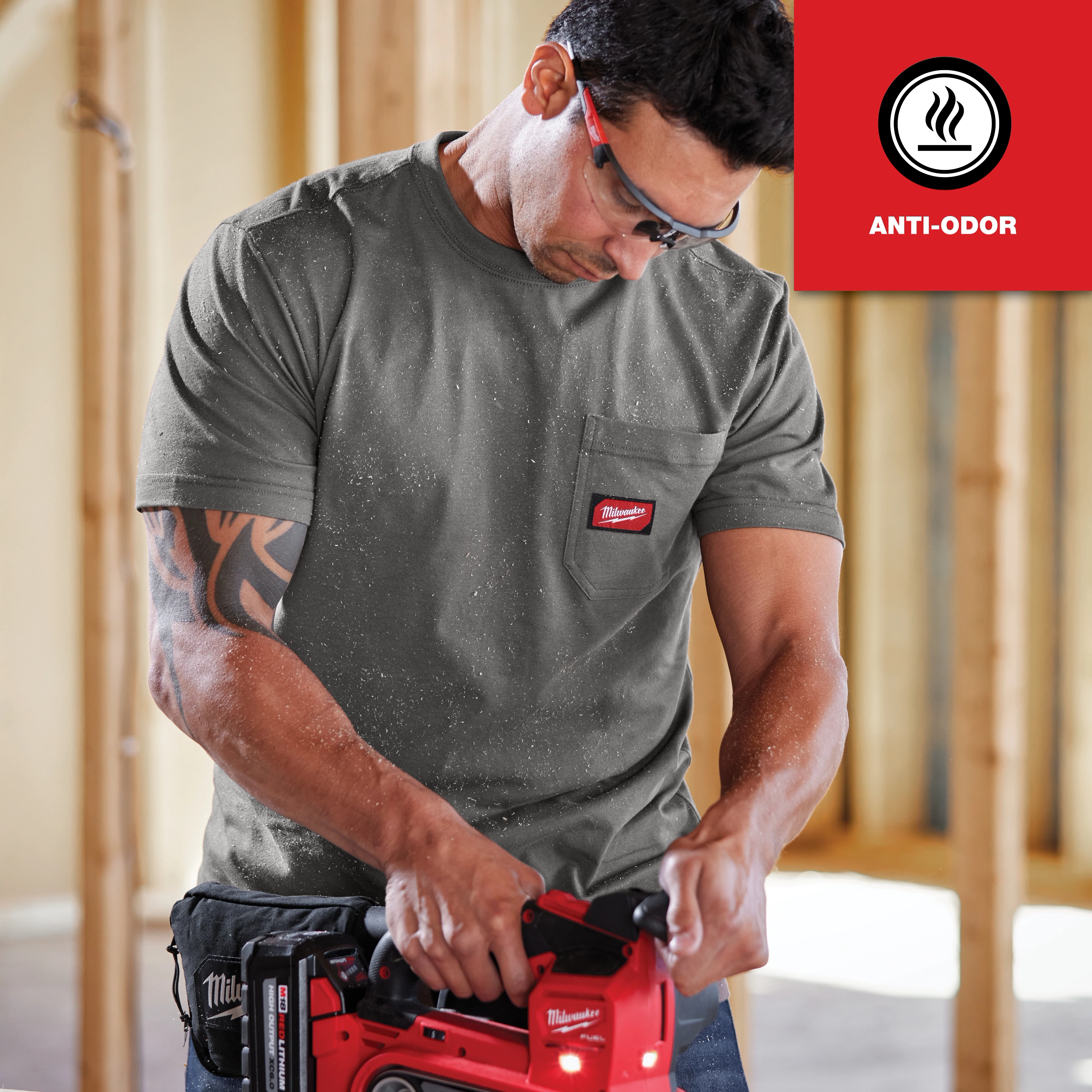 Man wearing a grey GRIDIRON Pocket T-Shirt - Short Sleeve Anti-odor while using a red power tool in a construction setting.