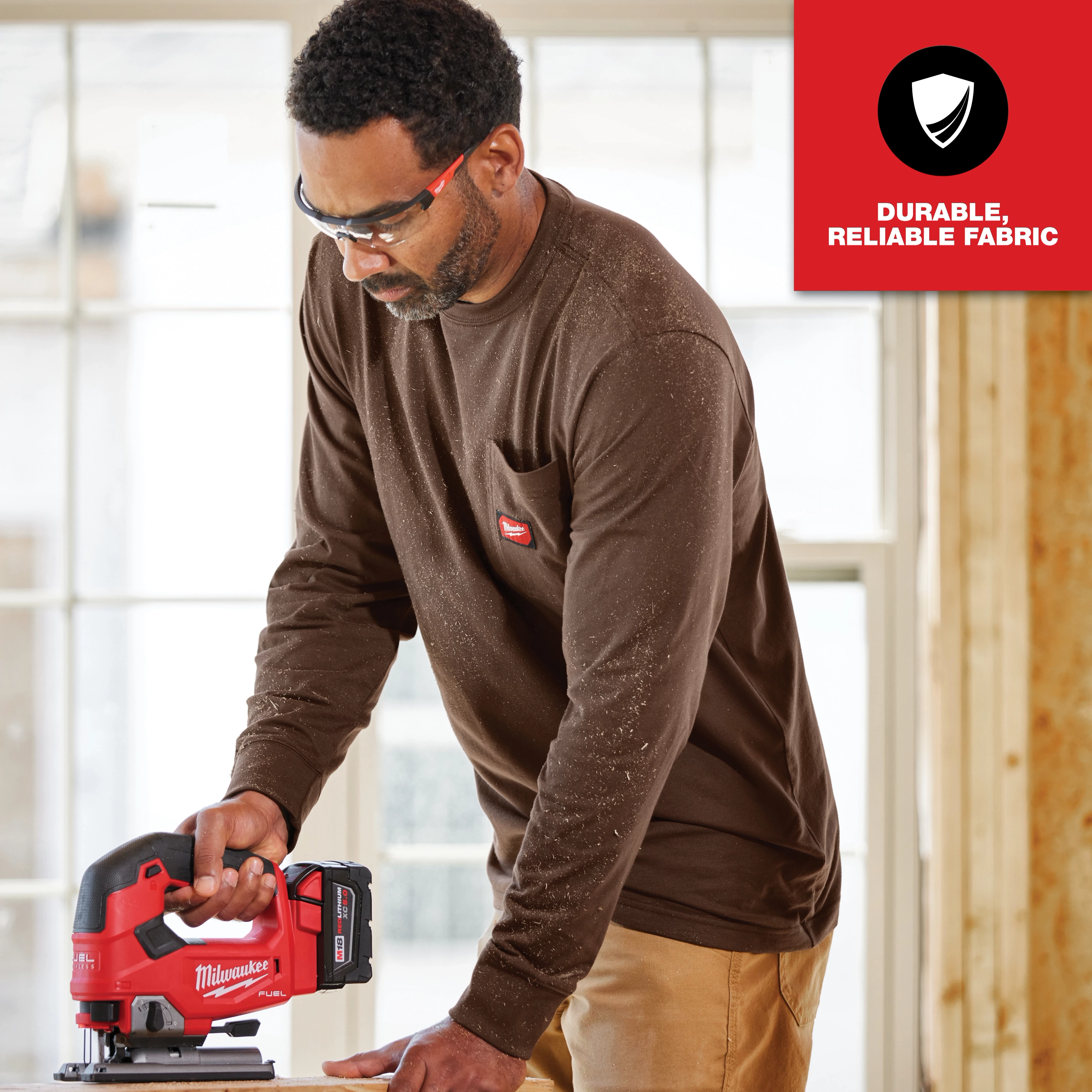 GRIDIRON Pocket T-Shirt - Long Sleeve, made from durable, reliable fabric, being worn by a person using a red power tool.