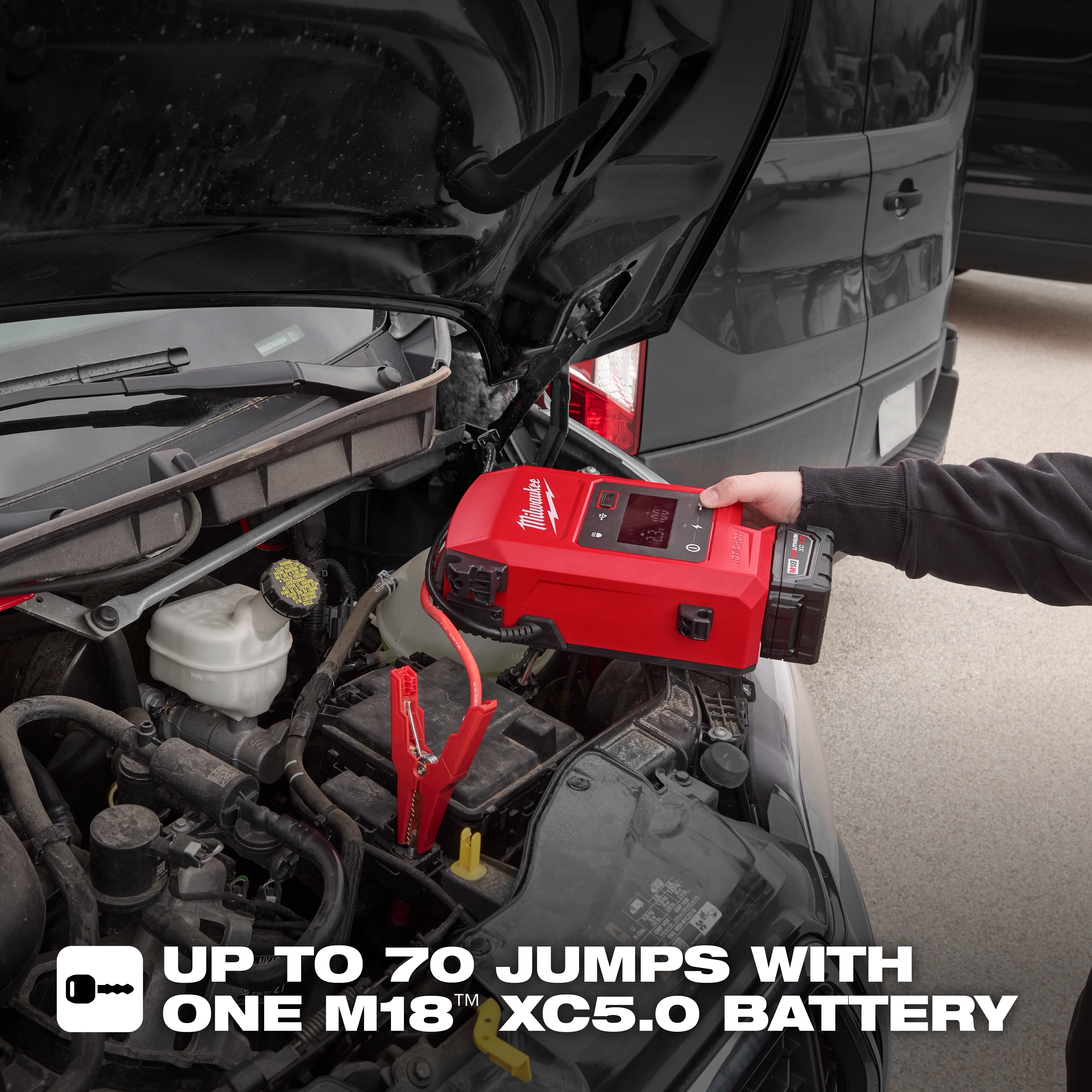 A person uses the M18™ HOTSHOT™ Jump Starter to charge a car battery. The device is red and black and the car hood is open. The text on the image states, "UP TO 70 JUMPS WITH ONE M18™ XC5.0 BATTERY."
