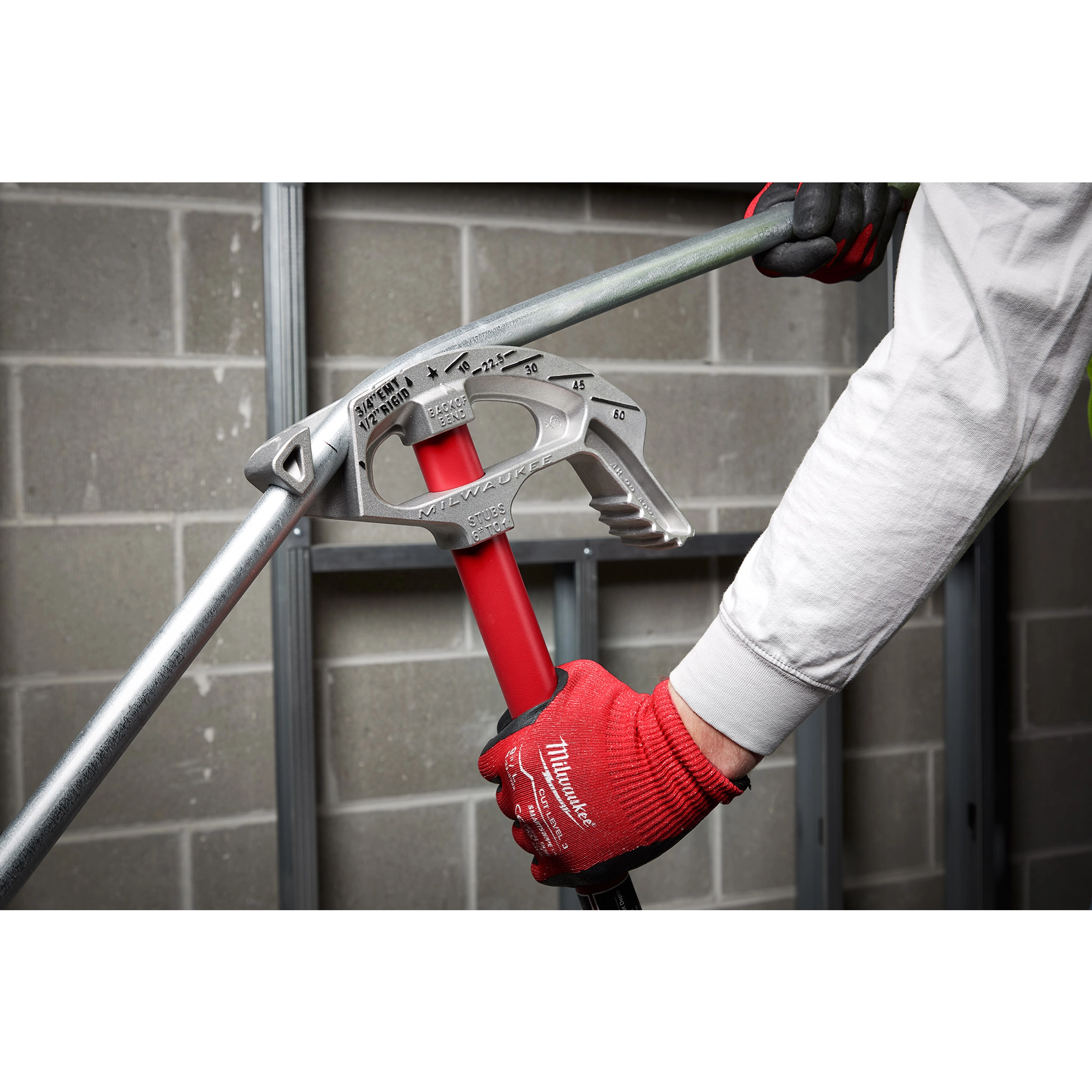 Person wearing red gloves using a 3/4" EMT Aluminum Conduit Bender to bend an electrical conduit in an unfinished room.
