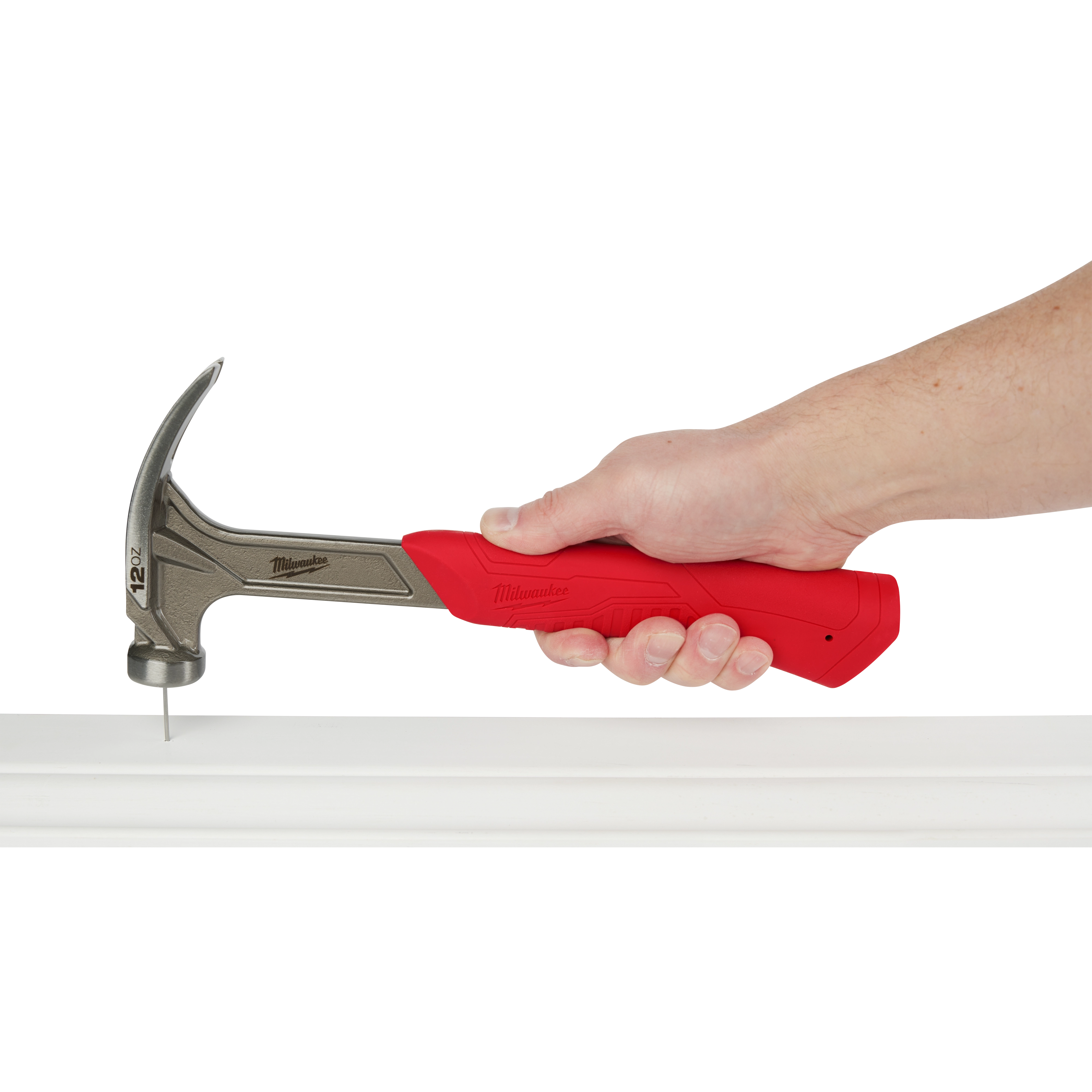 Hand holding a 12oz Smooth Face Hybrid Claw Finish Hammer with a red grip, hammering a nail into a white surface.