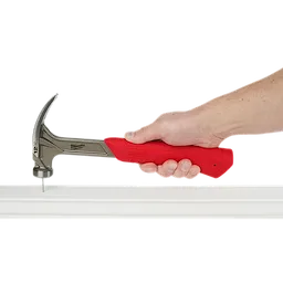 Hand holding a 12oz Smooth Face Hybrid Claw Finish Hammer with a red grip, hammering a nail into a white surface.