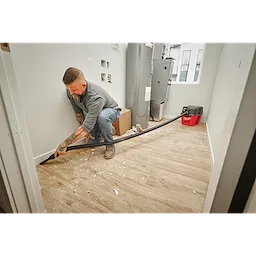 A person uses a shop vacuum with a 1-7/8” x 32” to 102” expandable hose to clean up construction debris from a floor.