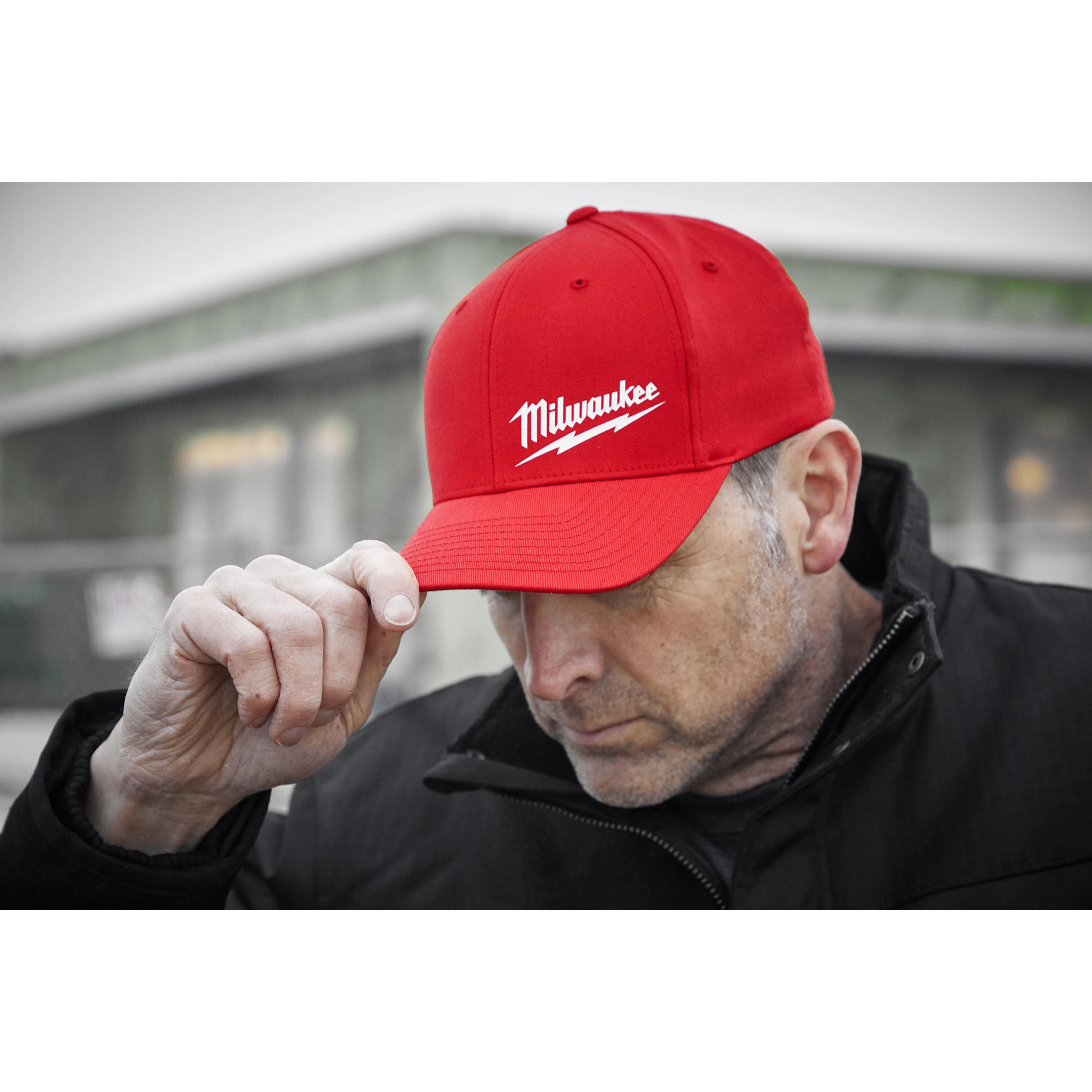 Person wearing a red Milwaukee Fitted Hat, with the Milwaukee logo prominently displayed, and a black jacket outdoors.