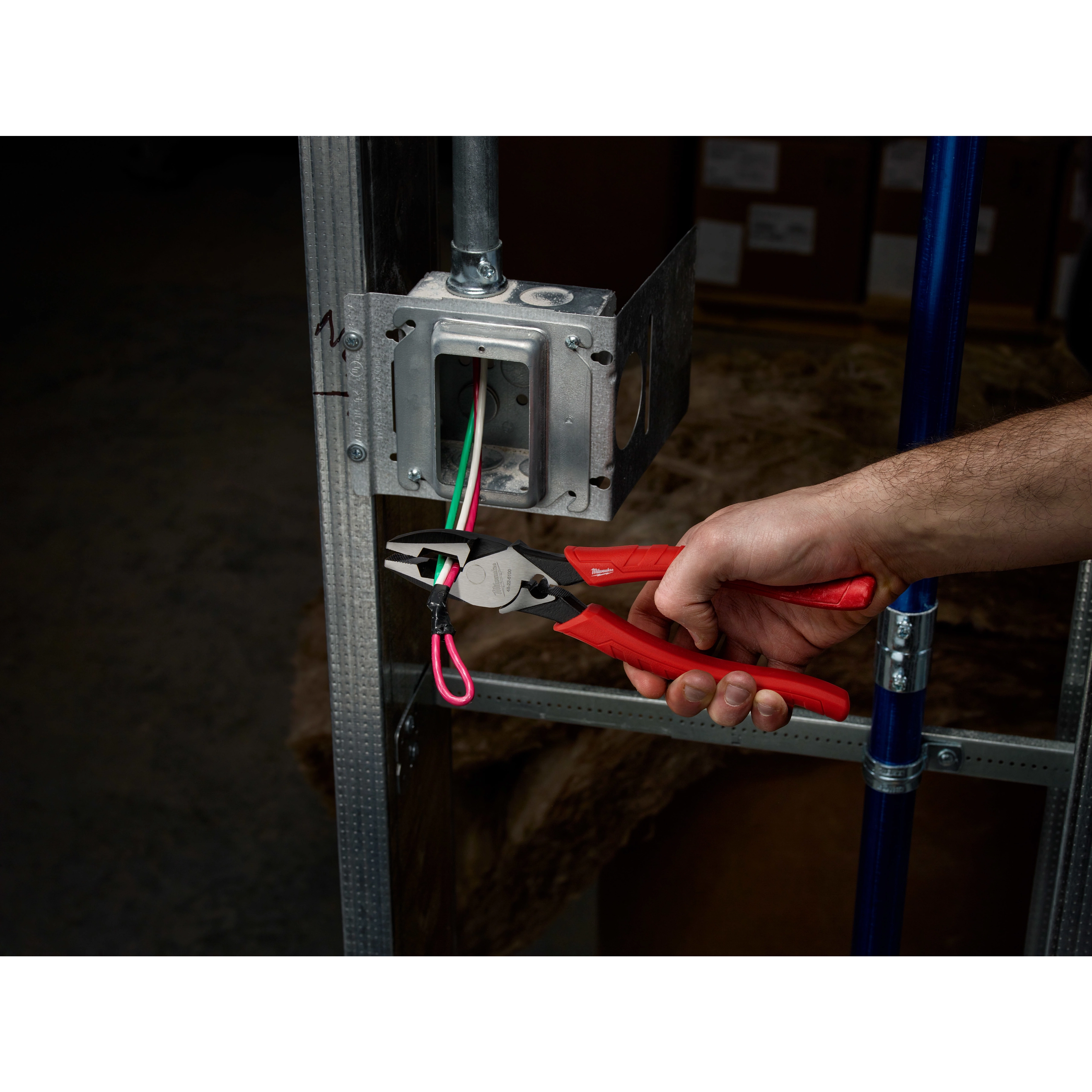 A person uses 9" High Leverage Lineman's Pliers With Crimper to grasp wires near an electrical box on a metal frame.