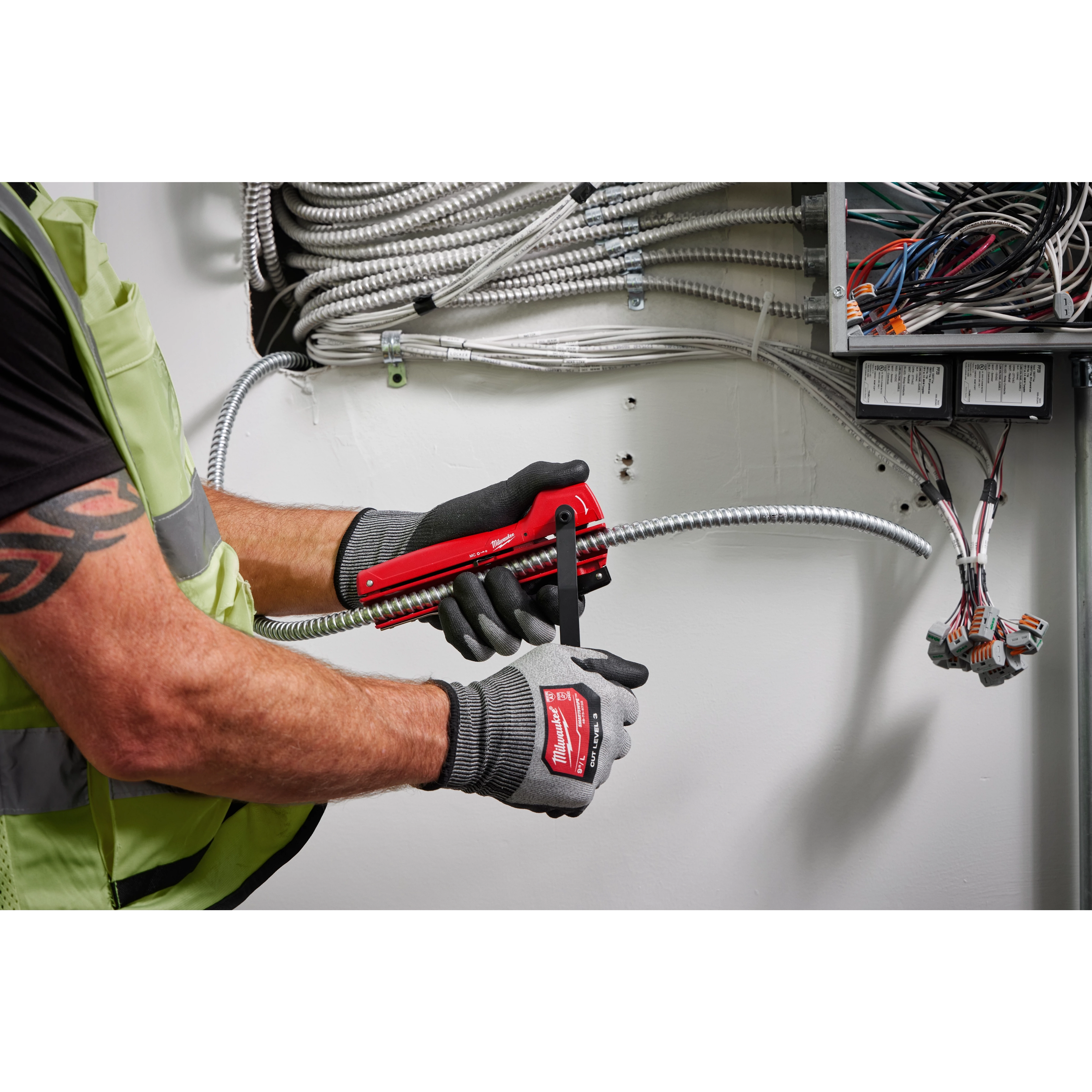 A person wearing gloves uses an Armored Cable Cutter to trim metallic conduit wires inside a control panel with multiple cables.