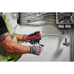 A person wearing gloves uses an Armored Cable Cutter to trim metallic conduit wires inside a control panel with multiple cables.