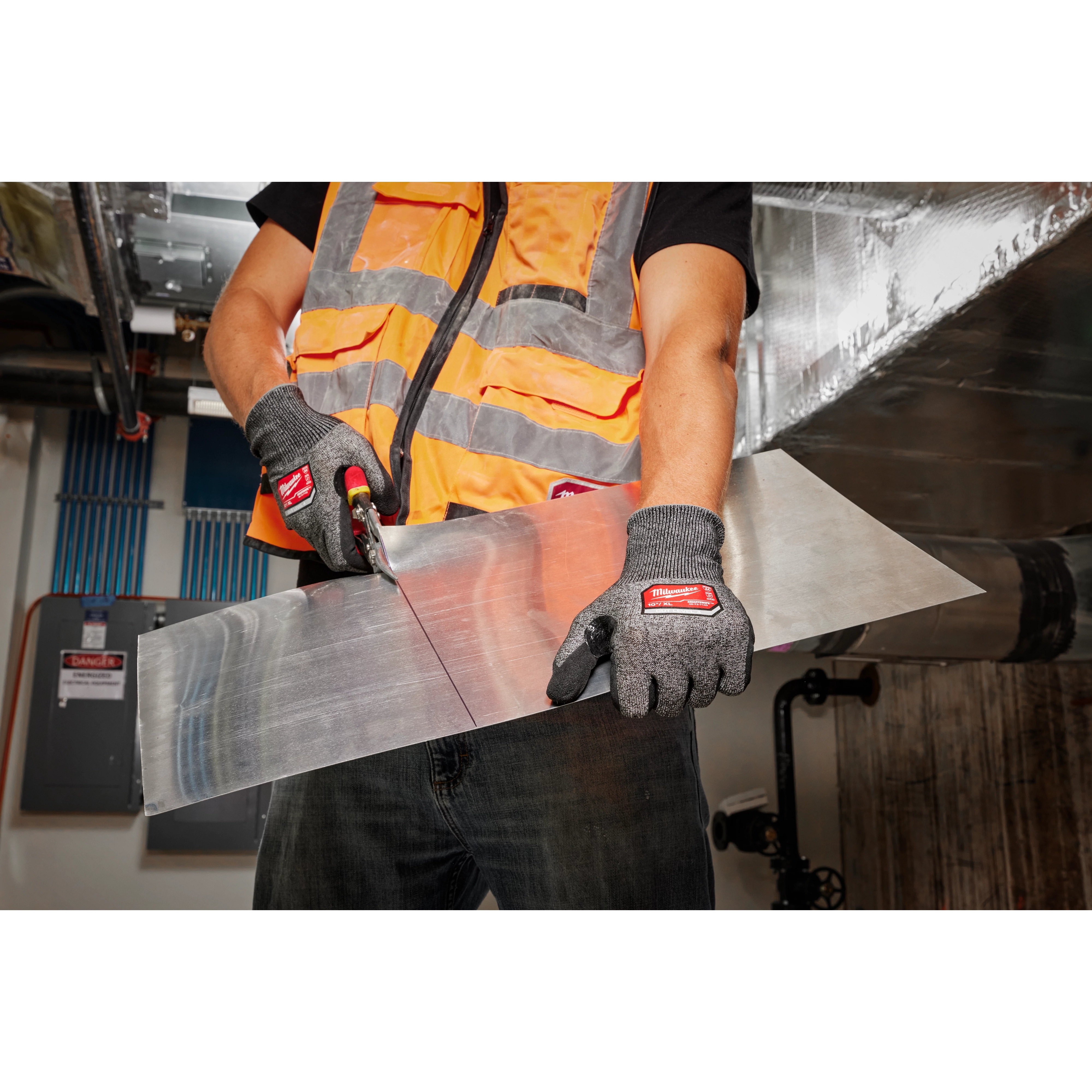 Worker wearing Cut Level 4 High-Dexterity Nitrile Dipped Gloves - XL, cutting a sheet of metal with snips in an industrial setting.