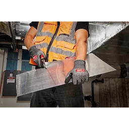Worker wearing Cut Level 4 High-Dexterity Nitrile Dipped Gloves - XL, cutting a sheet of metal with snips in an industrial setting.