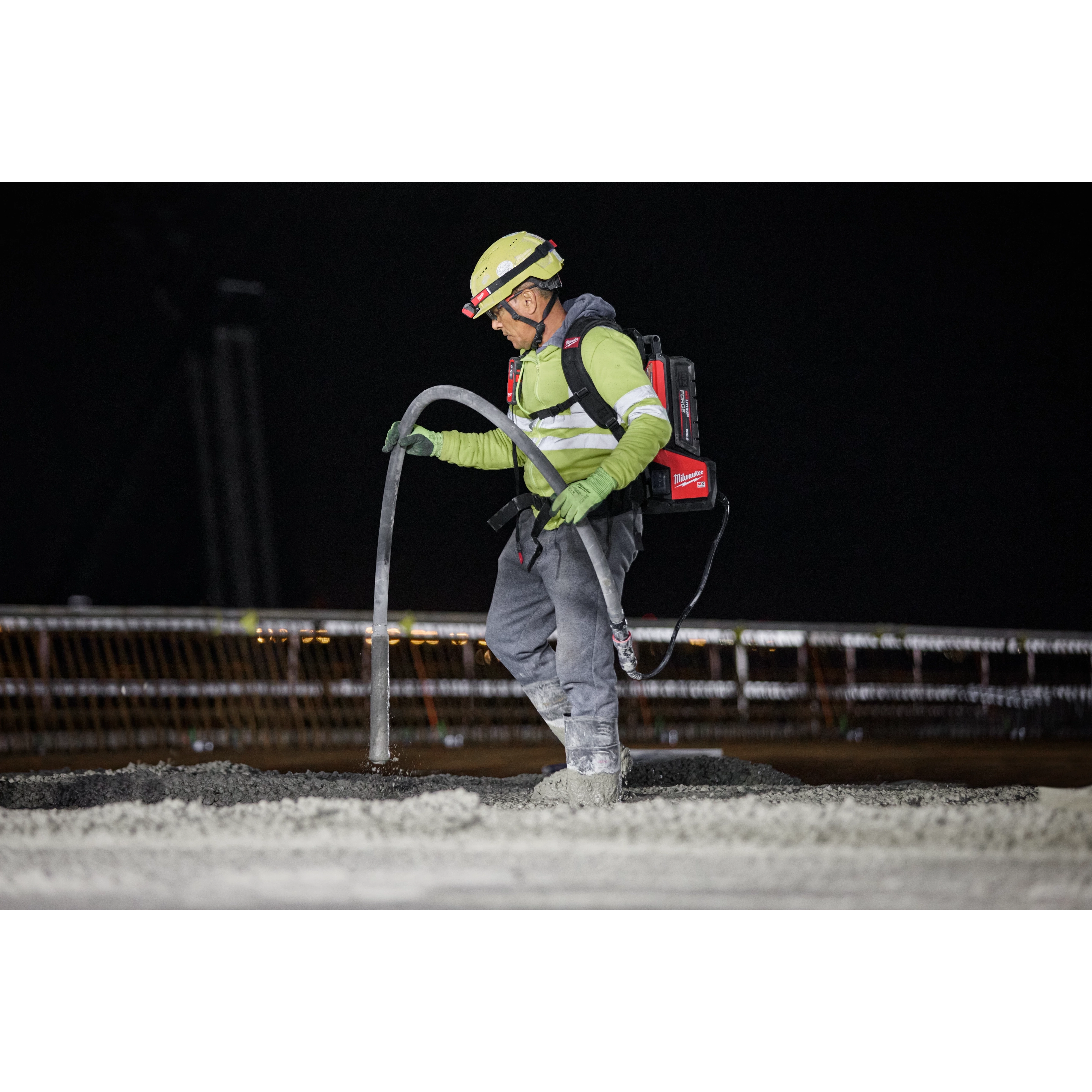 Worker operating MX FUEL High Cycle Concrete Vibrator while wearing facemask and safety gear, on a construction site at night.