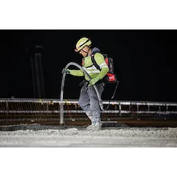 Worker operating MX FUEL High Cycle Concrete Vibrator while wearing facemask and safety gear, on a construction site at night.