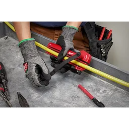 A person wearing safety gloves is using an Armored Cable Cutter to cut through a yellow cable on a workbench with tools nearby.
