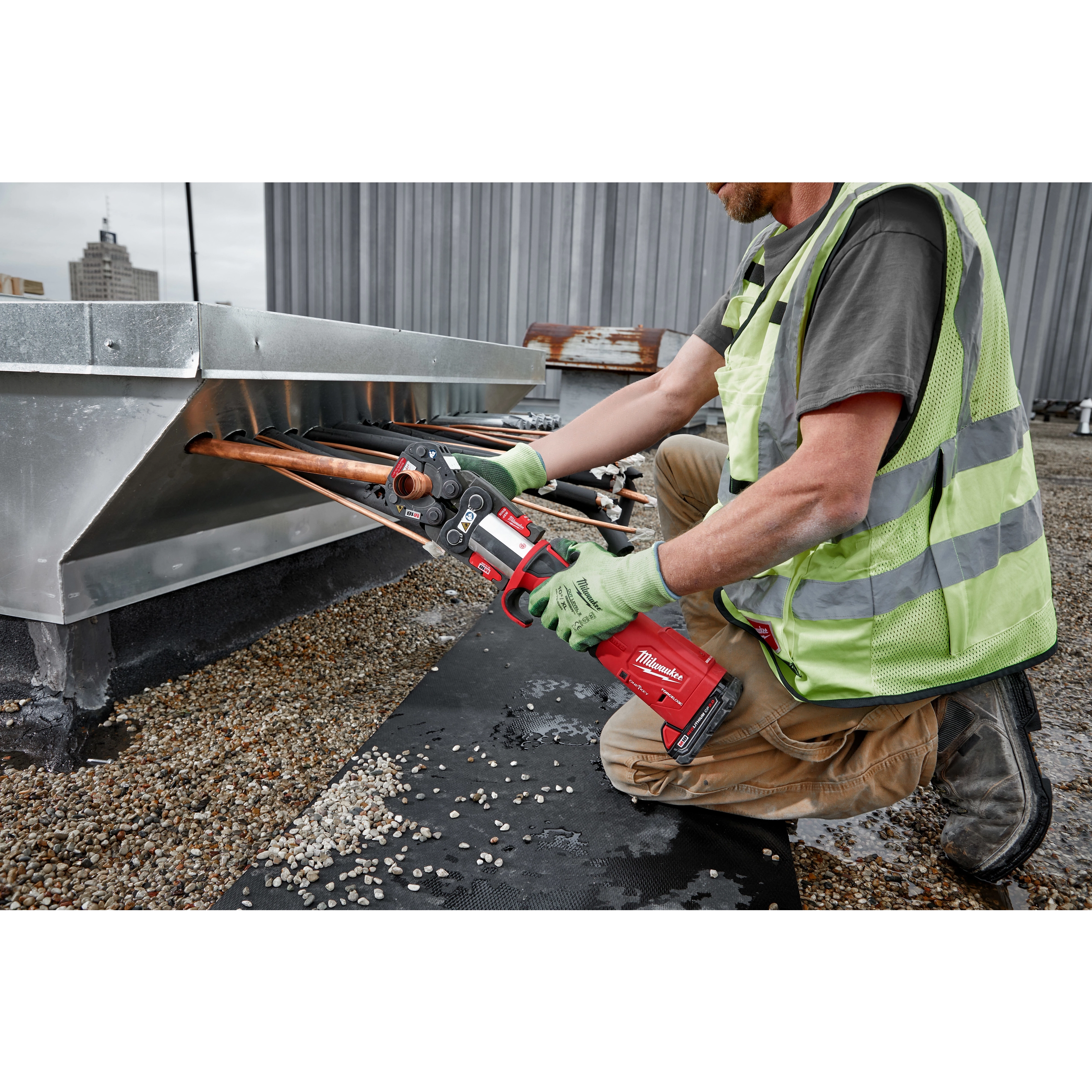 Worker using M18 FORCE LOGIC Press Tool Kit with One-Key and 1/4"-7/8" Streamline ACR Jaws on copper pipes on a rooftop.