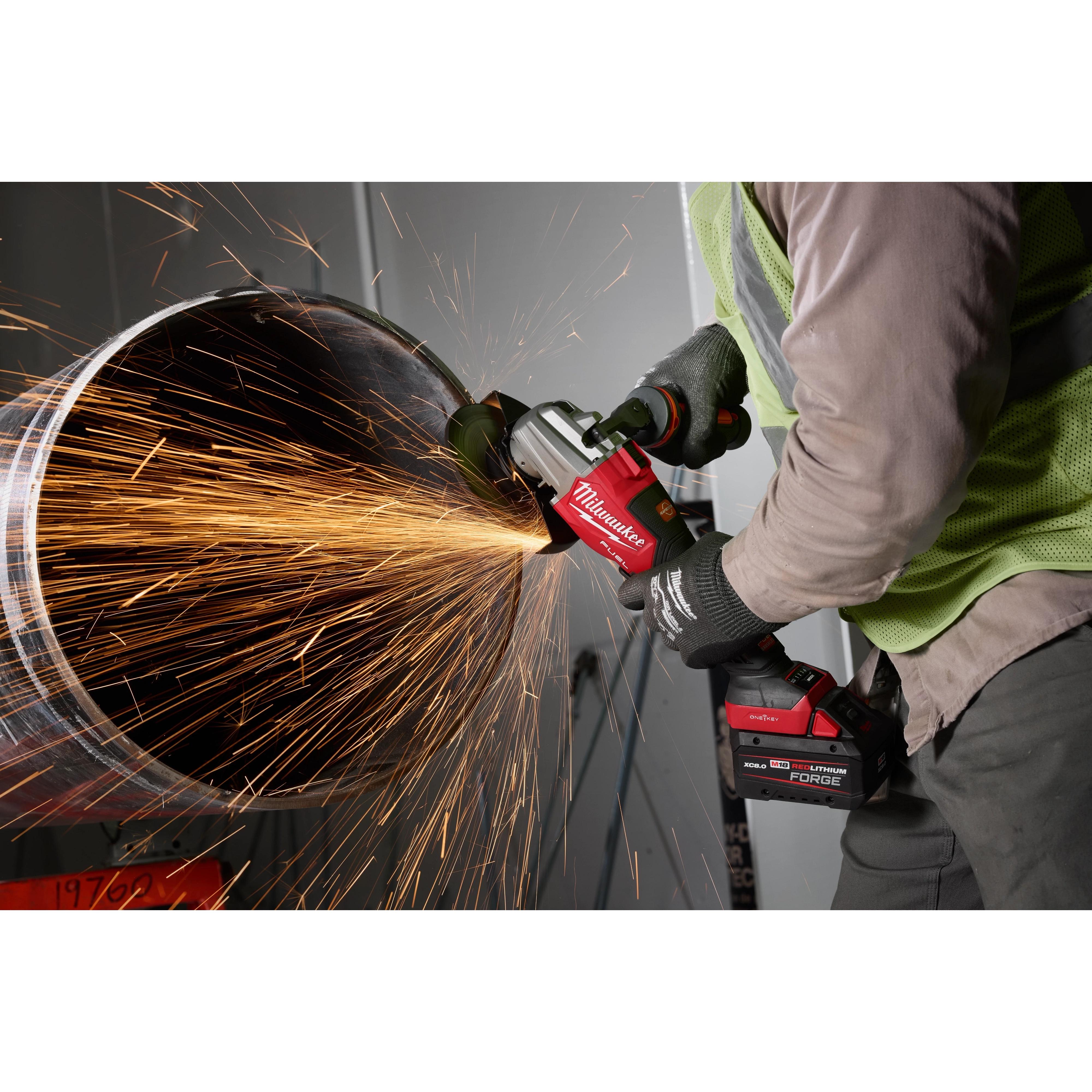 A person uses the M18 FUEL™ 4 1/2" - 6" Dual Trigger Braking Grinder, Paddle Switch w/ ONE KEY™ to cut through a metal pipe, producing bright sparks. The grinder is red with black accents and is held with both hands while wearing protective gloves.