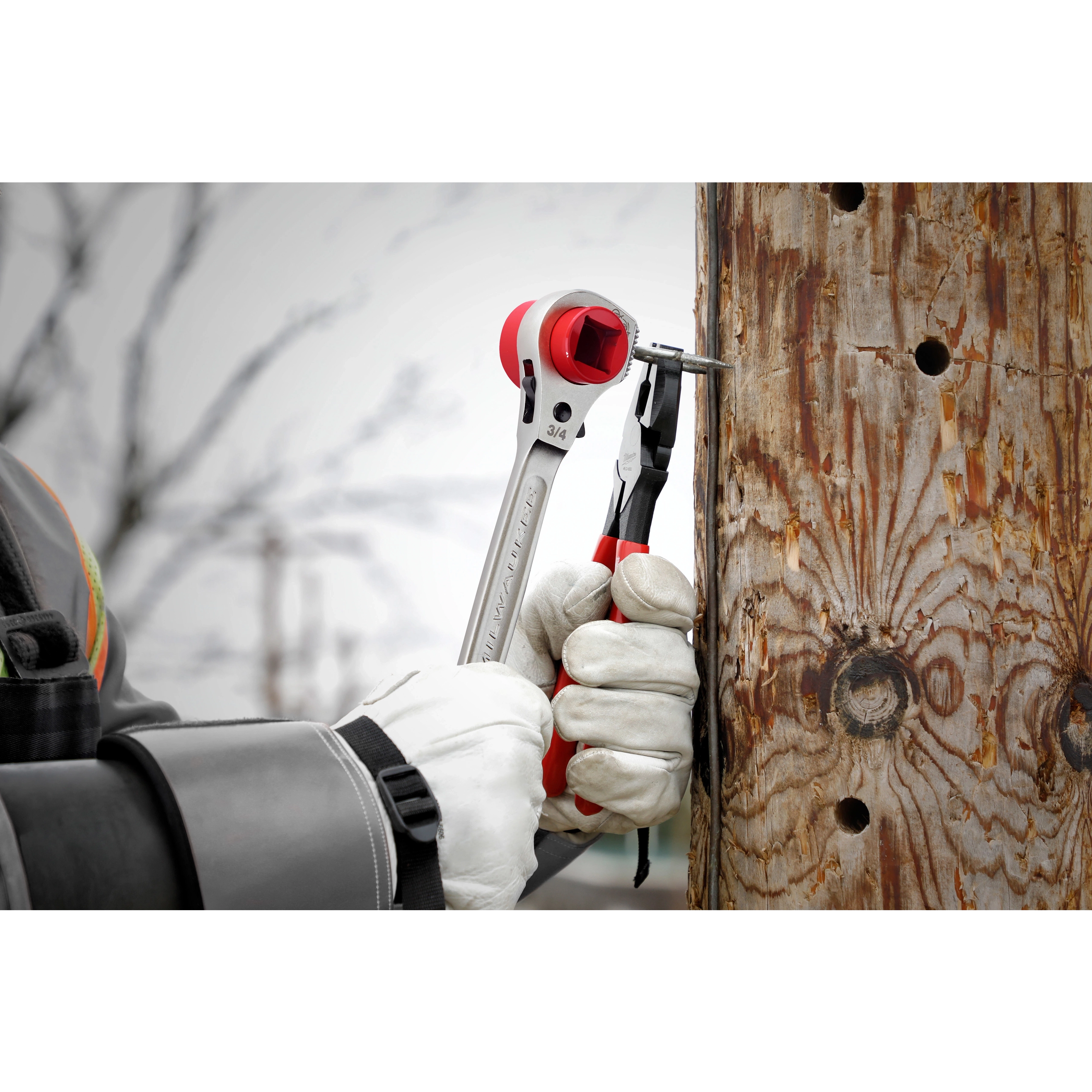 Lineman's 5IN1 Ratcheting Wrench with Milled Strike Face used by a person in gloves to tighten a nut on a wooden utility pole.