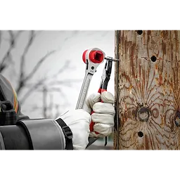 Lineman's 5IN1 Ratcheting Wrench with Milled Strike Face used by a person in gloves to tighten a nut on a wooden utility pole.