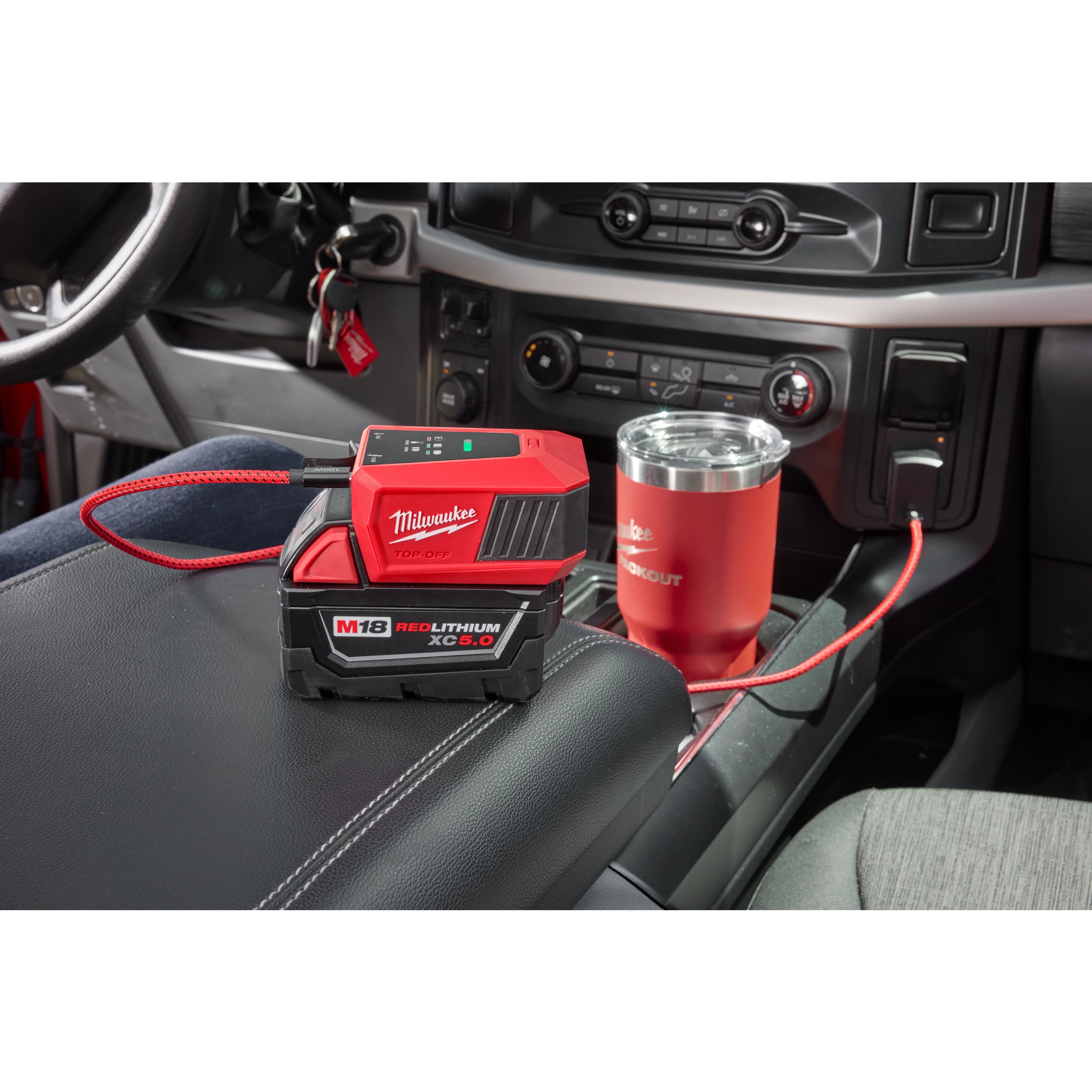 The M18™ TOP-OFF™ Charger & Power Supply is shown inside a car, placed on the center console, connected via a USB cable, with a red tumbler. The device is attached to an M18 REDLITHIUM XC 5.0 battery.