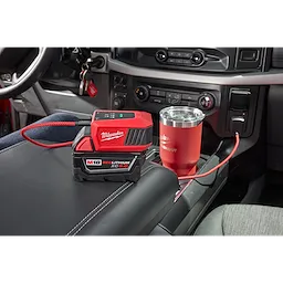 The M18™ TOP-OFF™ Charger & Power Supply is shown inside a car, placed on the center console, connected via a USB cable, with a red tumbler. The device is attached to an M18 REDLITHIUM XC 5.0 battery.