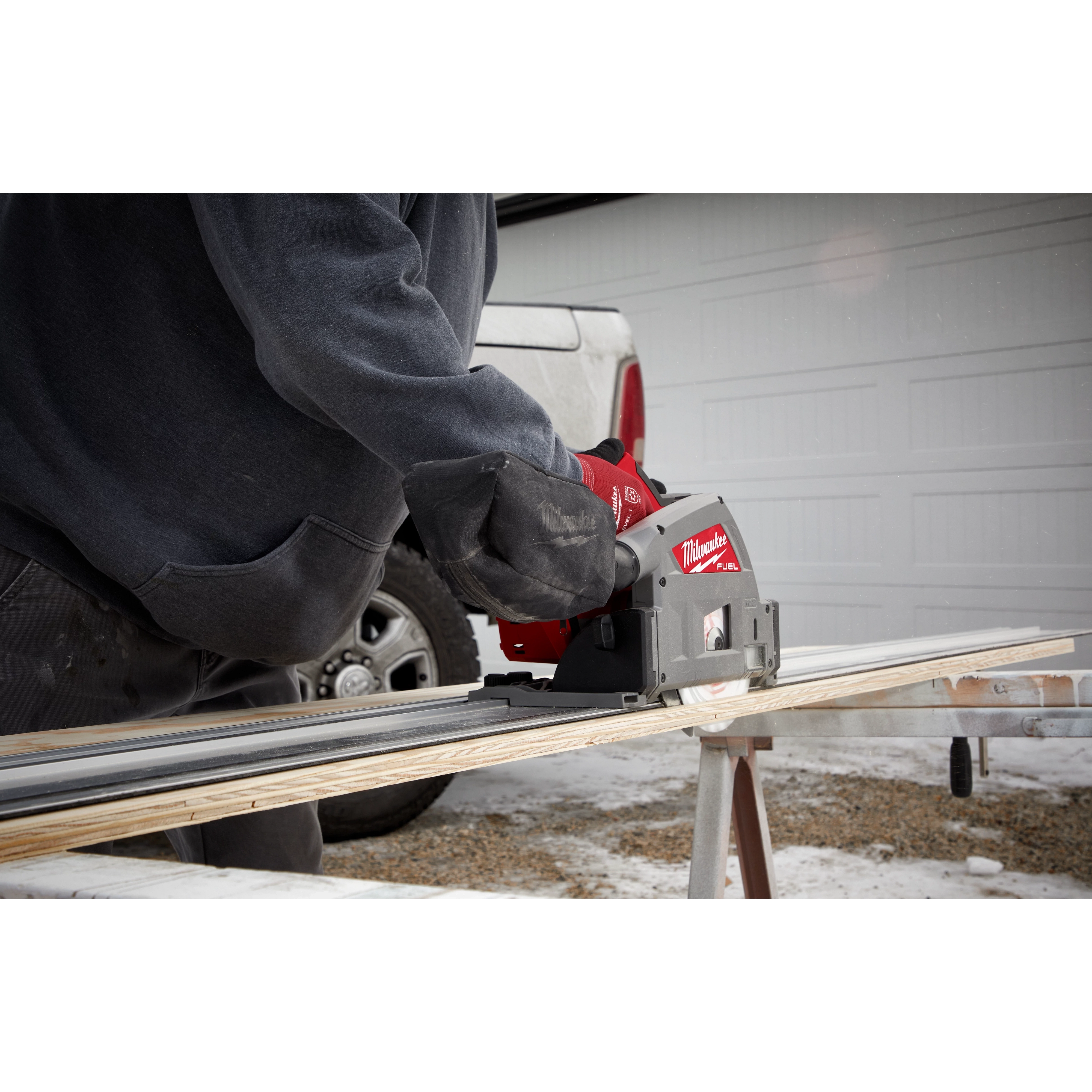 Person using the M18 FUEL 6 1/2" Plunge Track Saw to cut a wooden board outdoors on a portable workbench.