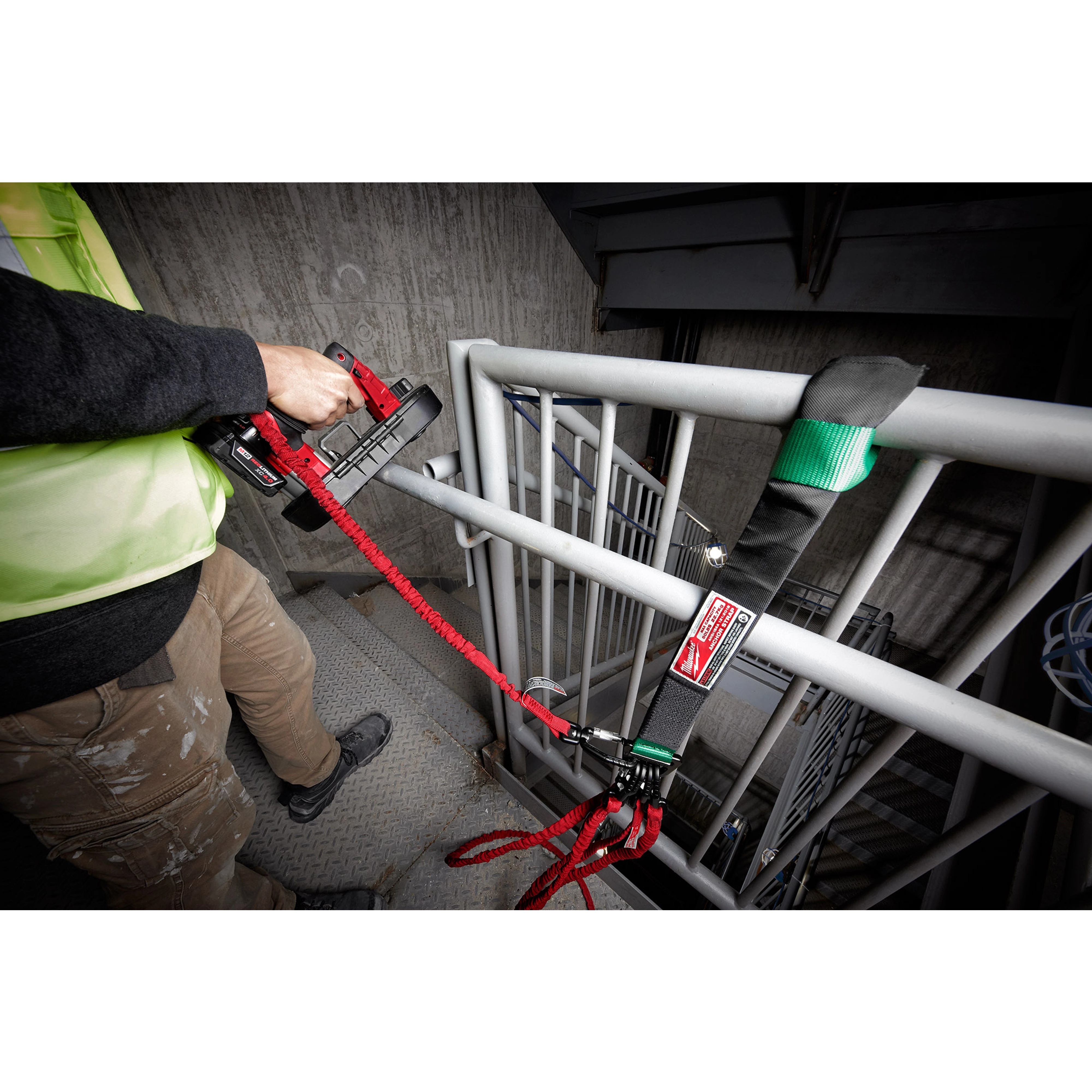 Worker uses a tool to secure the 50LBS Anchor Strap to a railing on a metal staircase, ensuring safety and stability.