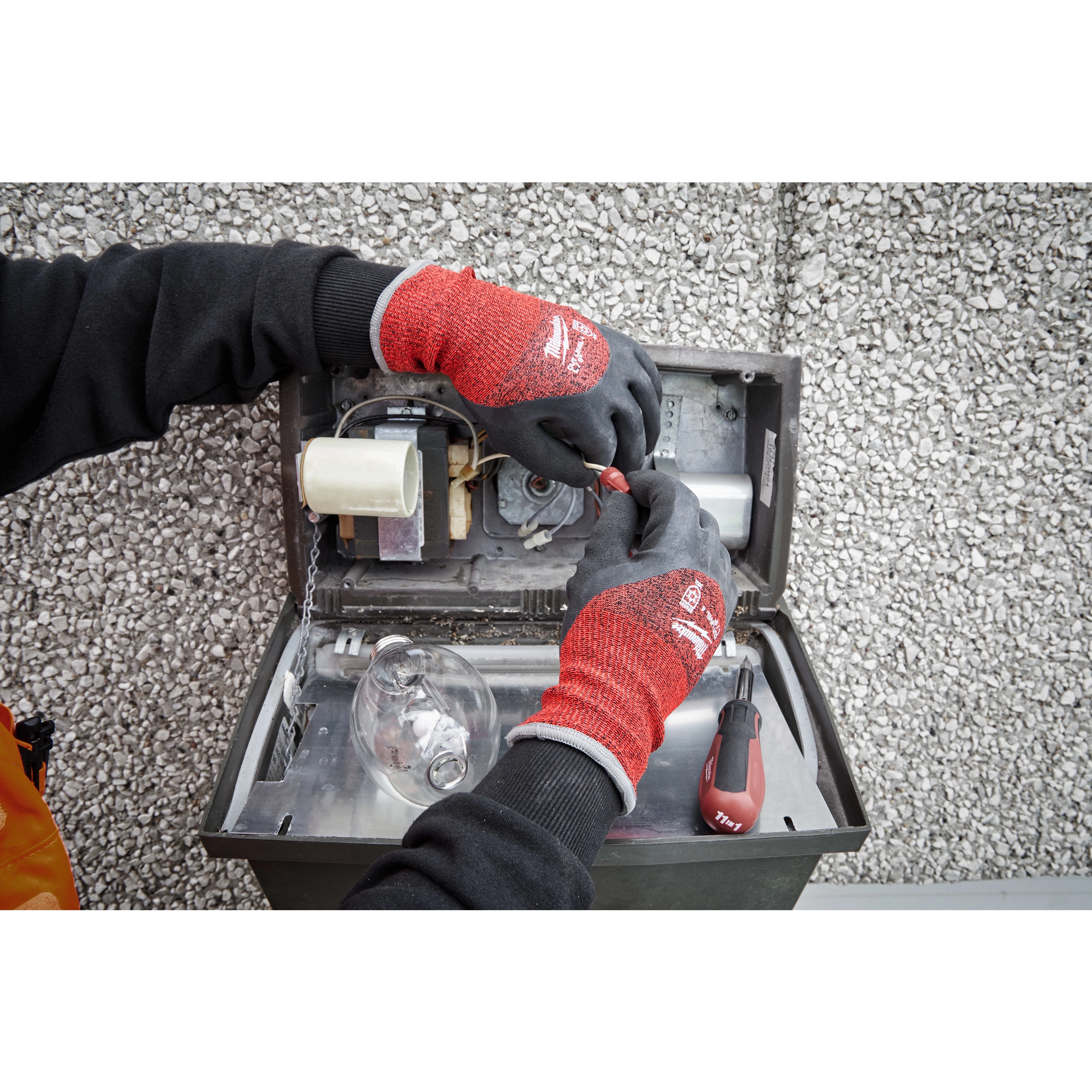 Person wearing Cut Level 4 Winter Dipped Gloves - L working on electrical components, with hands inside an open metal box.