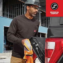 A person wearing a long-sleeve GRIDIRON Pocket T-Shirt in a construction setting, standing near an open vehicle tailgate and holding a safety vest.