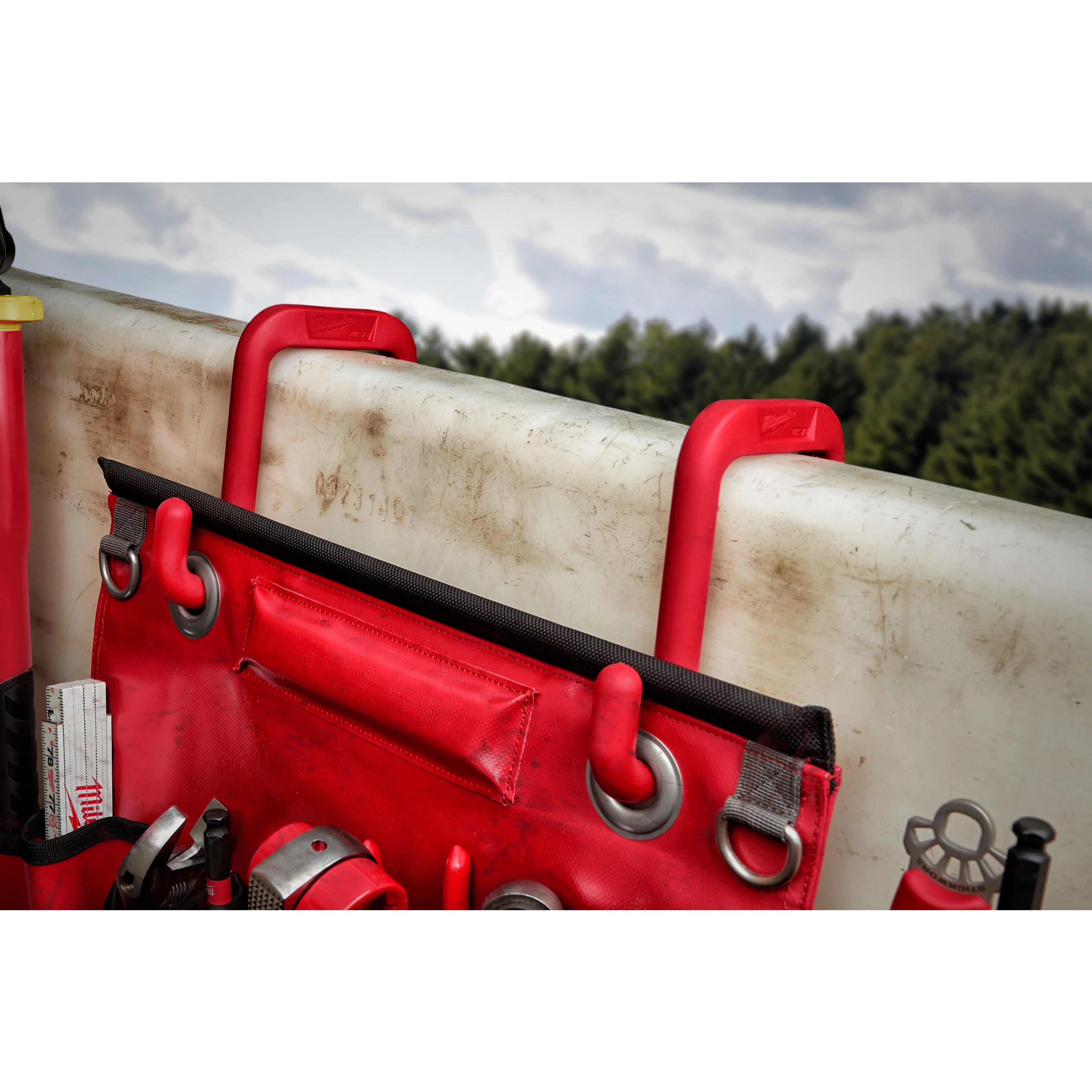 2" Bucket Hooks in red are mounted on the rim of a white surface, holding a red tool apron with various tools and accessories.