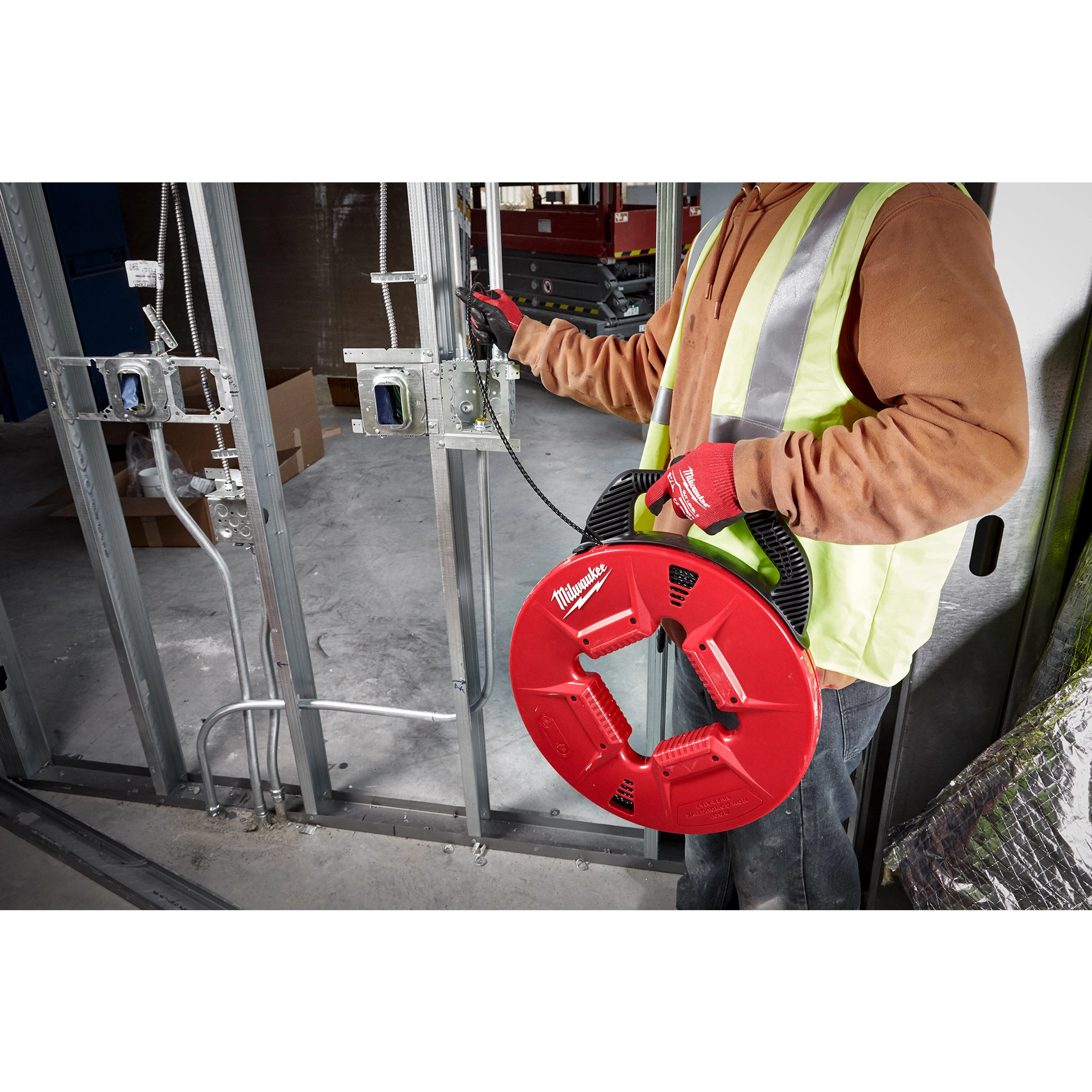 Worker using 200% Polyester Fish Tape with Non-conductive tip in a construction setting, wearing a yellow vest and red gloves.