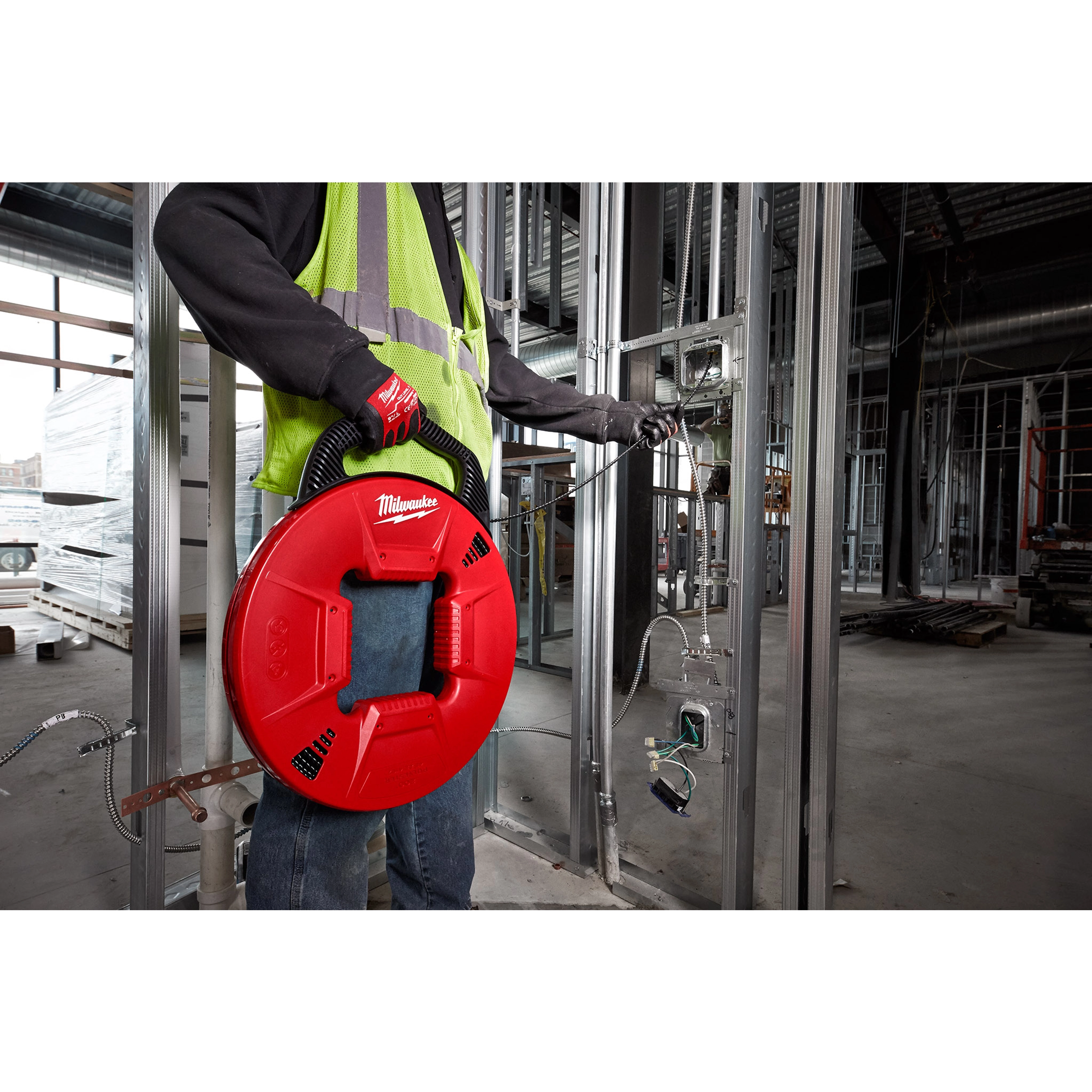 Person wearing gloves and a safety vest holds a red 200% Polyester Fish Tape with Flexible Leader in a construction setting.