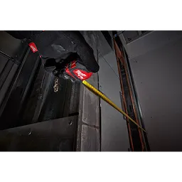 Gloved hand holding a red 10ft/3 Keychain Tape Measure with LED, extending the yellow tape while working on a metal surface.